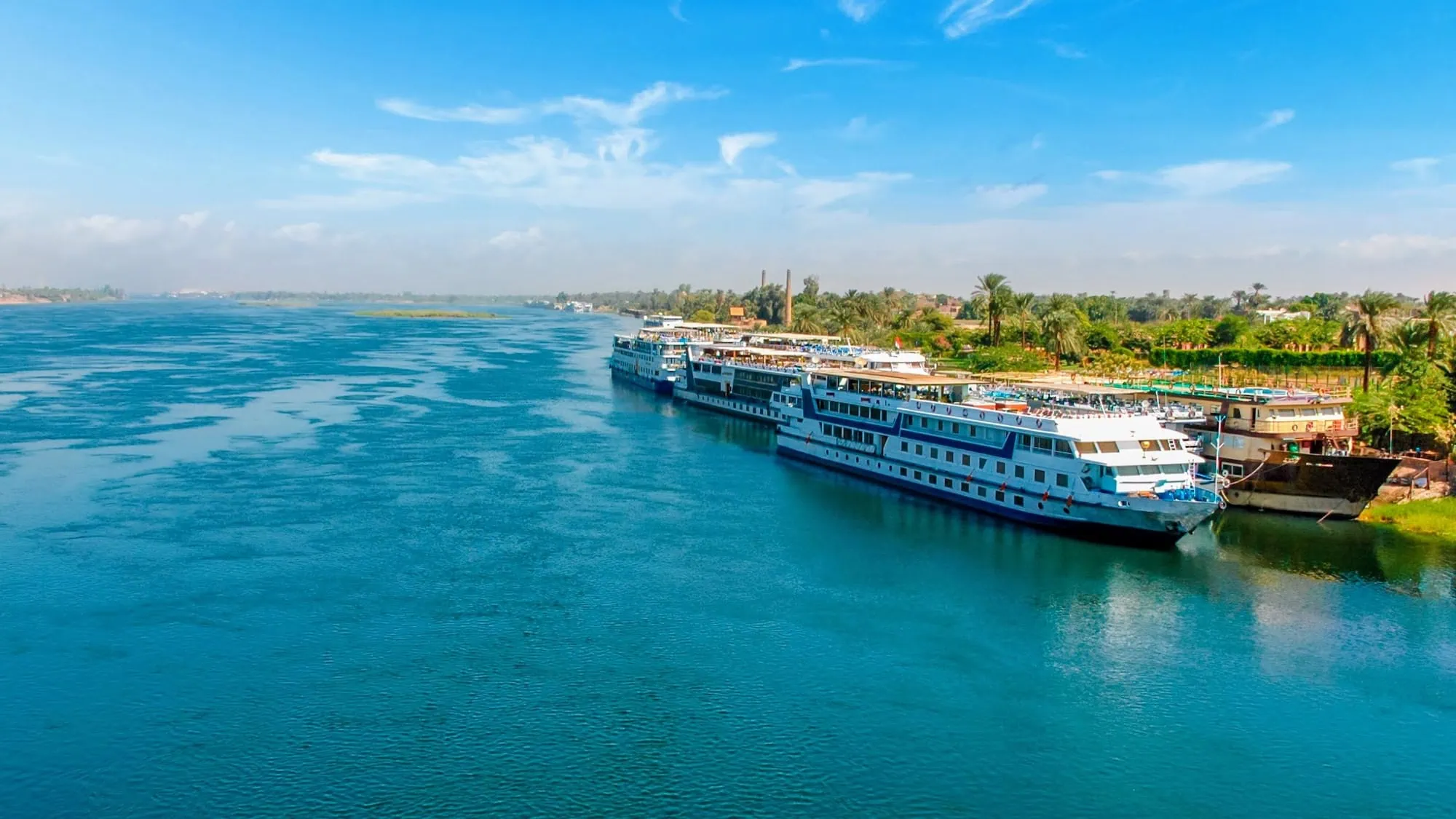 Large white cruise ship docked along the Nile River with lush vegetation