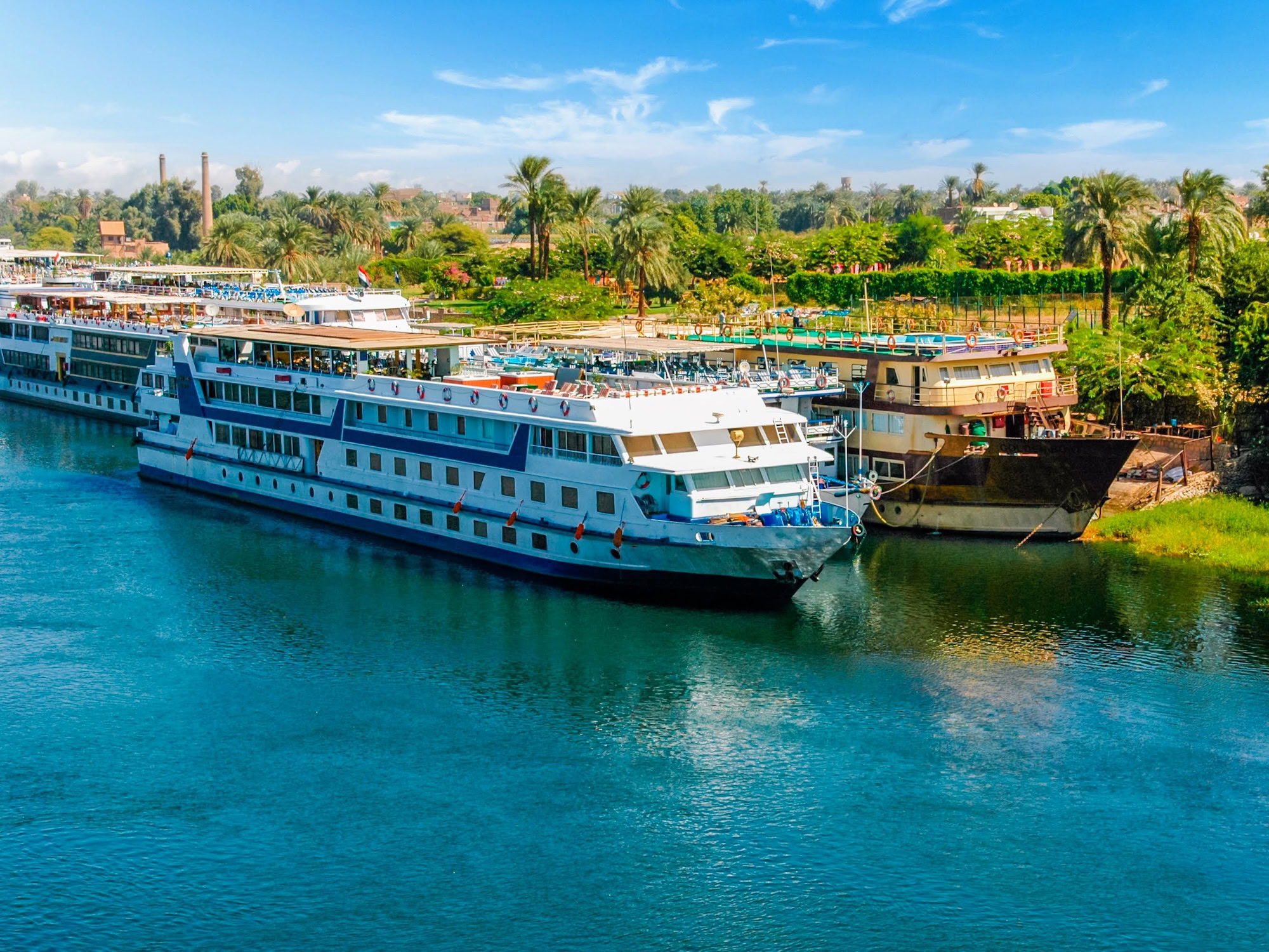 Nile River cruise boats docked along the riverbank with palm trees and desert landscape