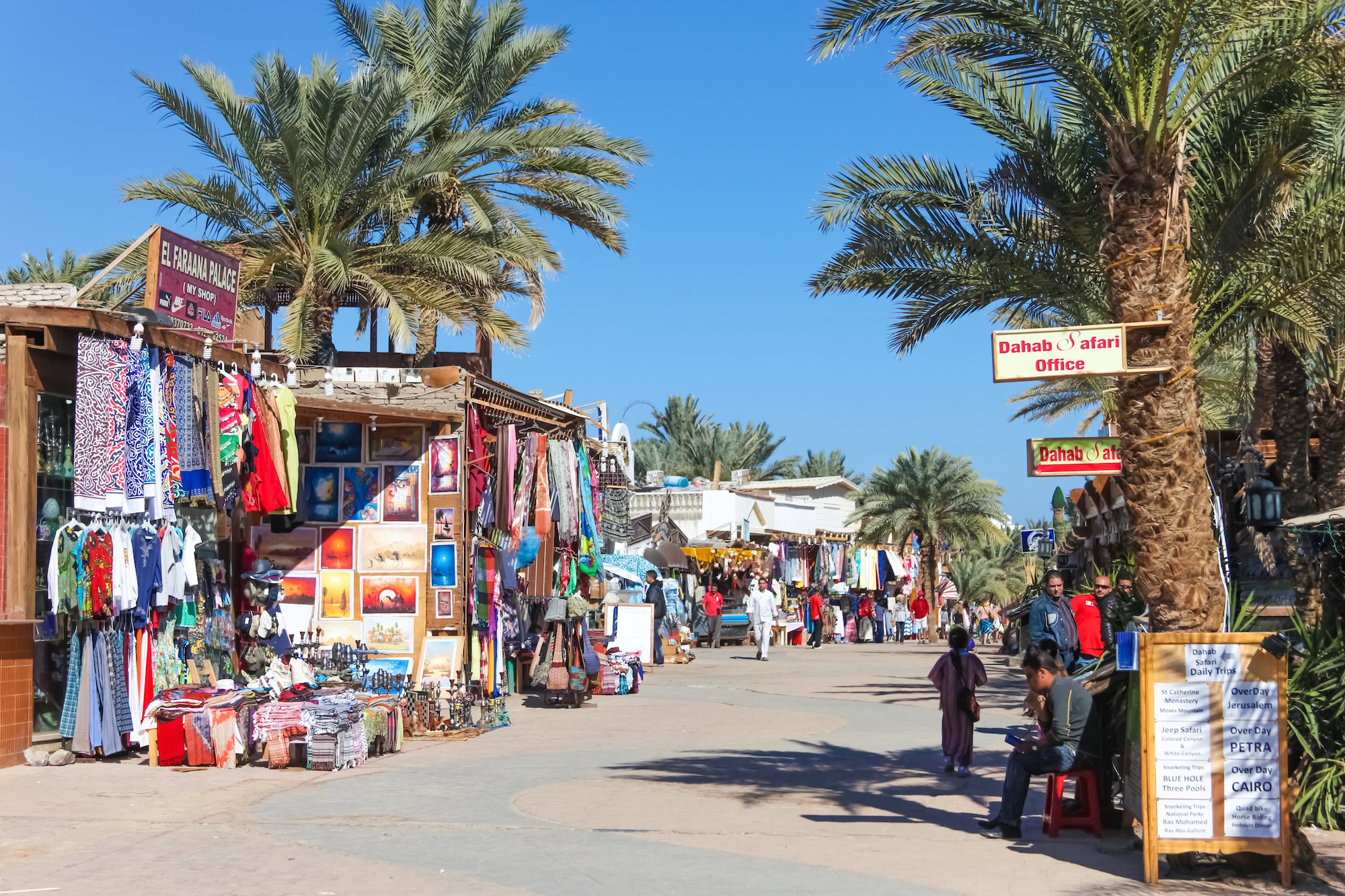 Vibrant Dahab marketplace with palm trees, market stalls, and tourists browsing souvenirs and textiles