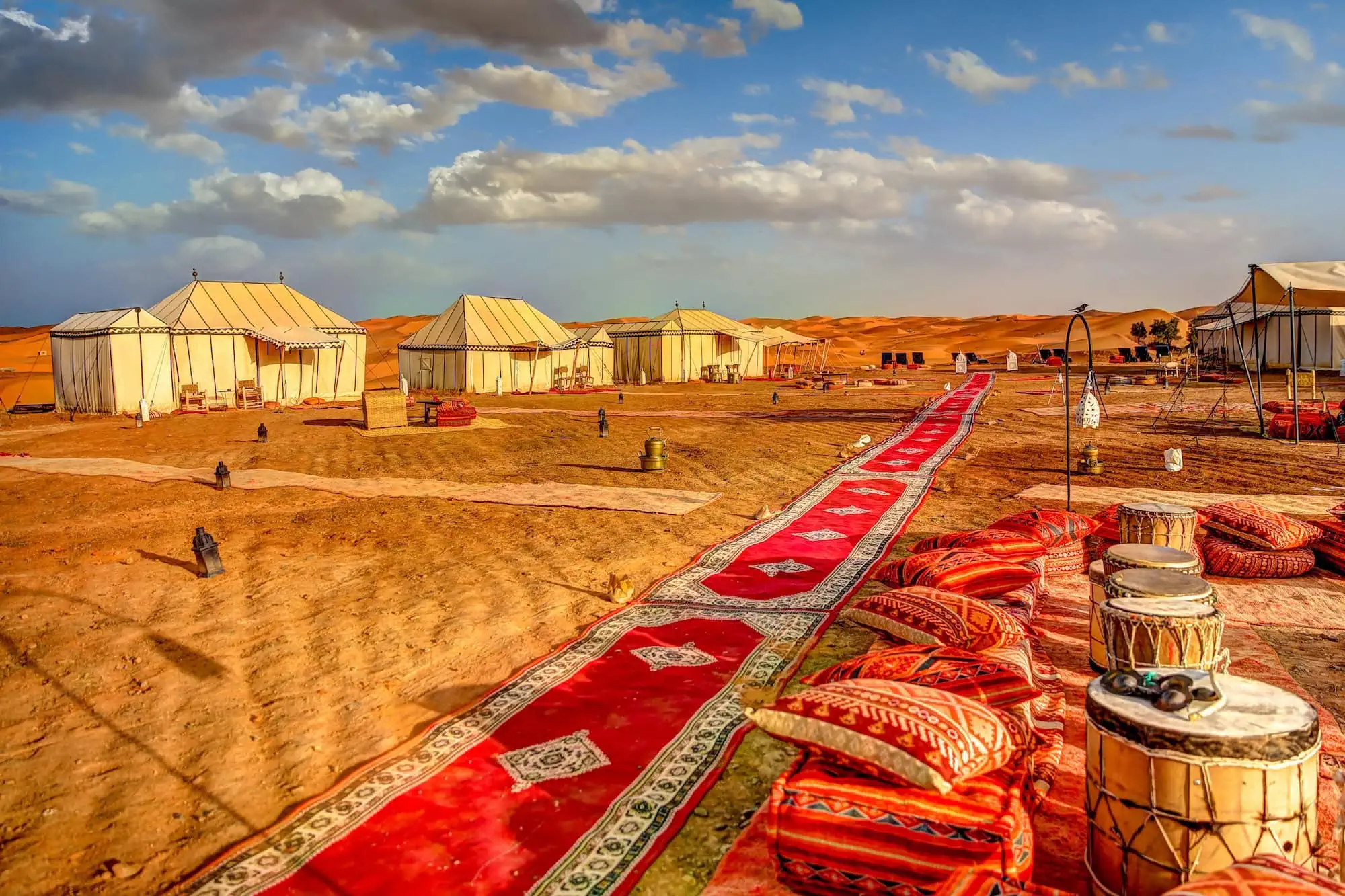 Traditional Bedouin desert camp with ornate tents, carpets, and lanterns under cloudy desert sky