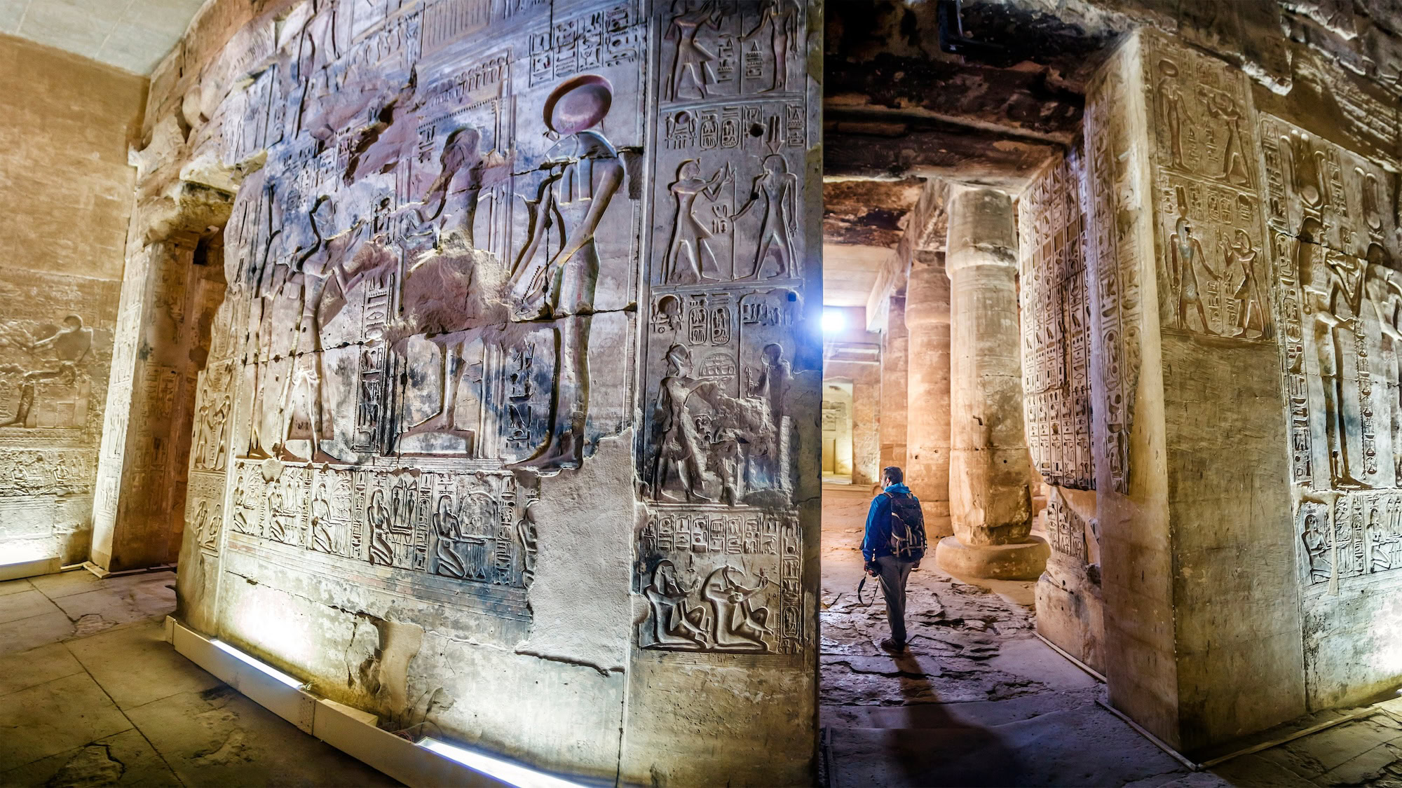 Visitor examining ancient hieroglyphic wall carvings in Egyptian temple interior