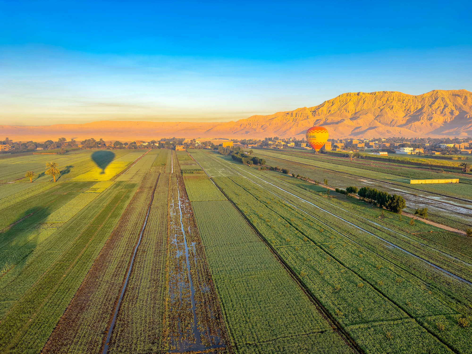 Hot air balloons floating over agricultural fields and farmland near Luxor with mountains in the background