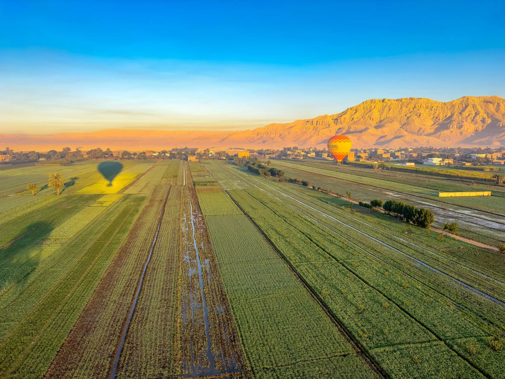 Hot air balloons floating over agricultural fields and farmland near Luxor with mountains in the background