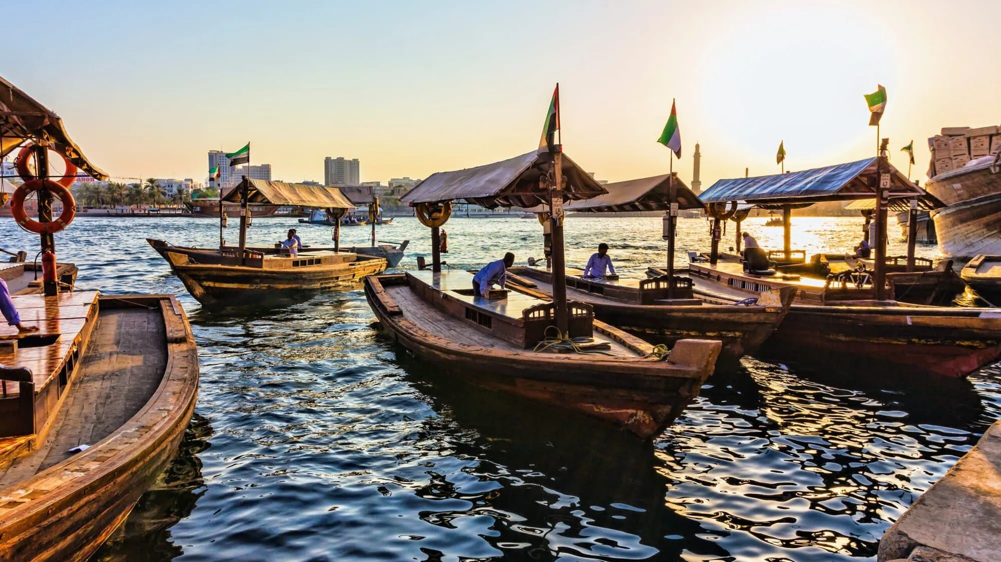 Traditional Abra boats docked at Dubai Creek with city skyline in background