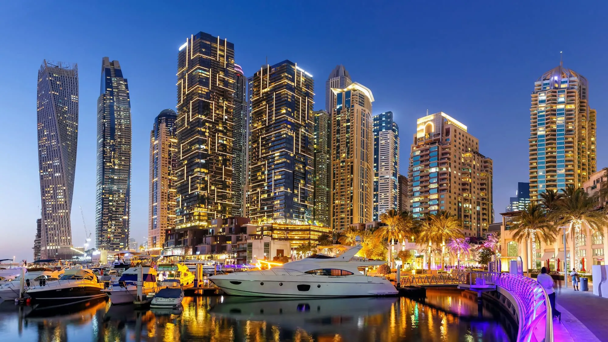 Dubai Marina with illuminated skyscrapers, yachts, and boats reflecting in the water at evening