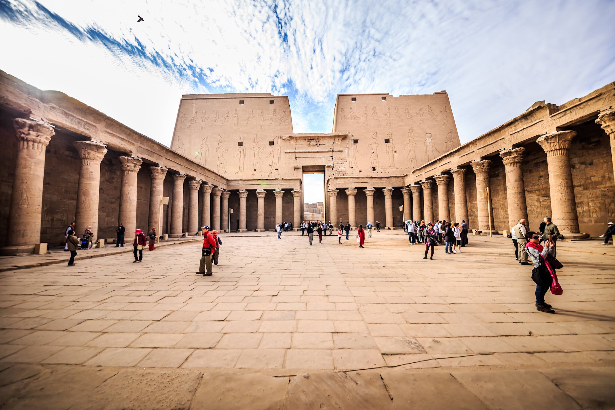 Tourists exploring the ancient Temple of Horus in Edfu with massive sandstone columns and hieroglyphic walls