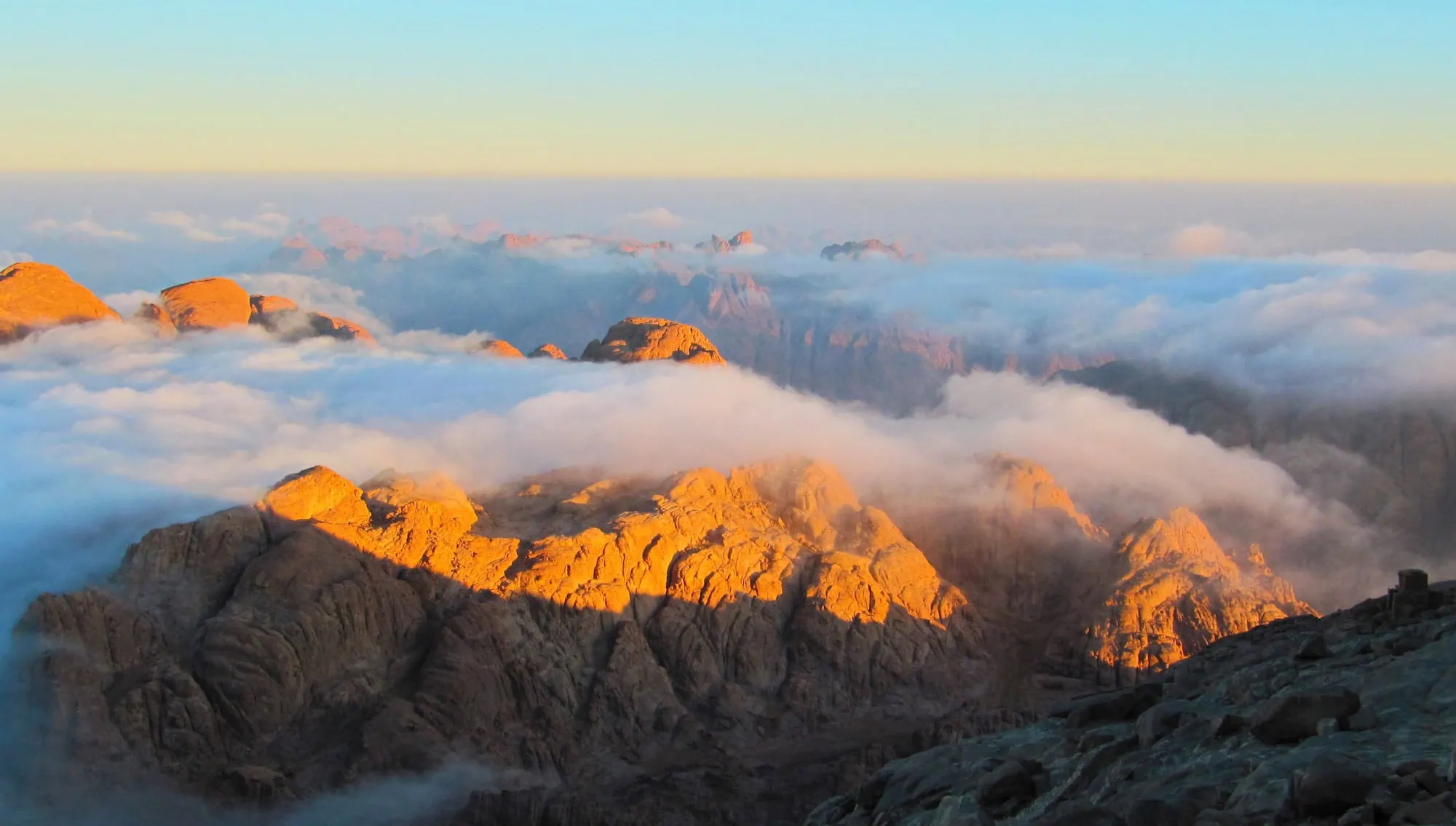 Breathtaking sunrise view from Mount Sinai summit showing golden mountain peaks emerging from white clouds
