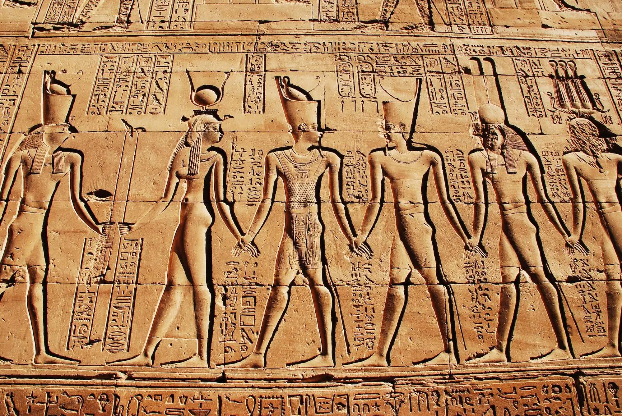 Ancient Egyptian temple wall relief showing hieroglyphics and carved figures of deities and pharaohs