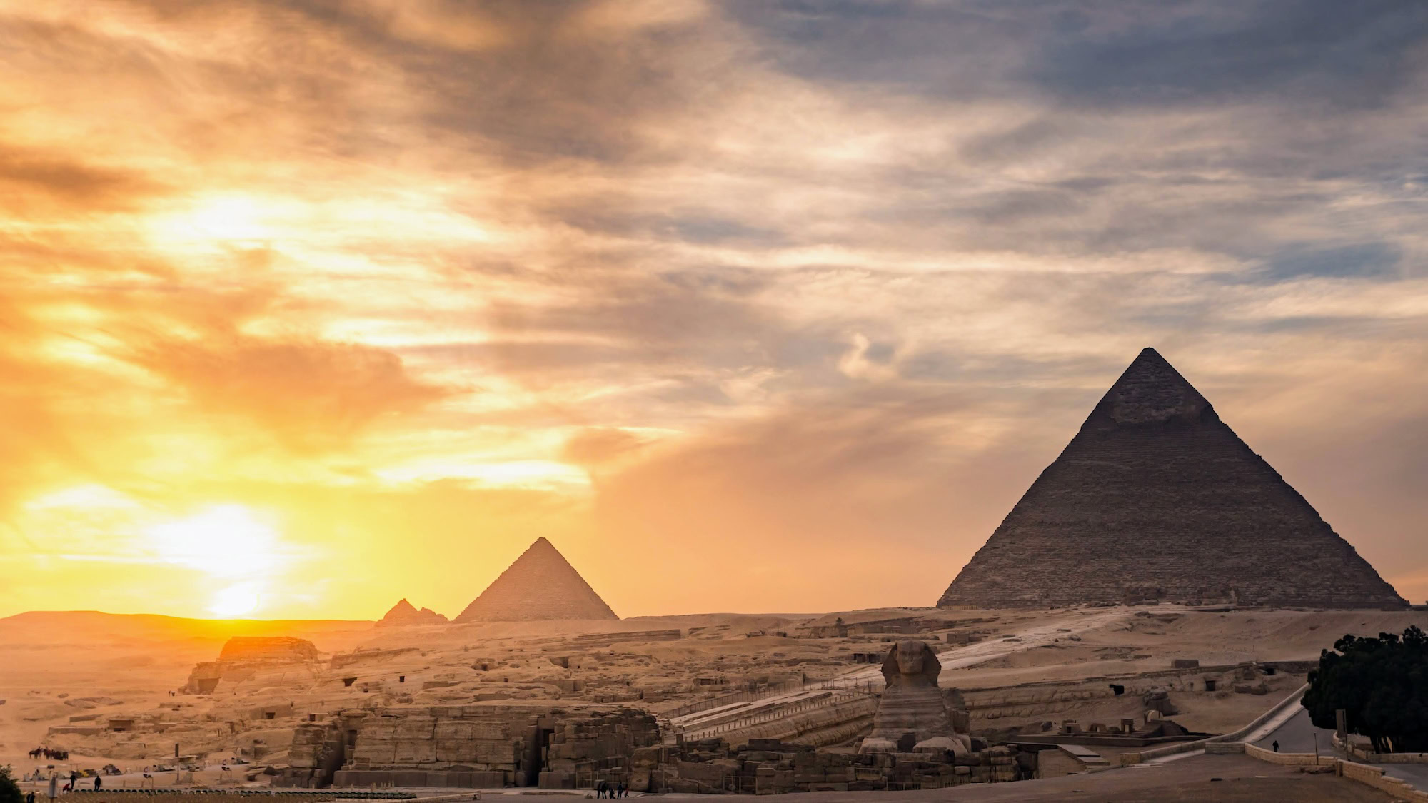 Panoramic sunset view of the Giza pyramid complex with dramatic orange and blue sky