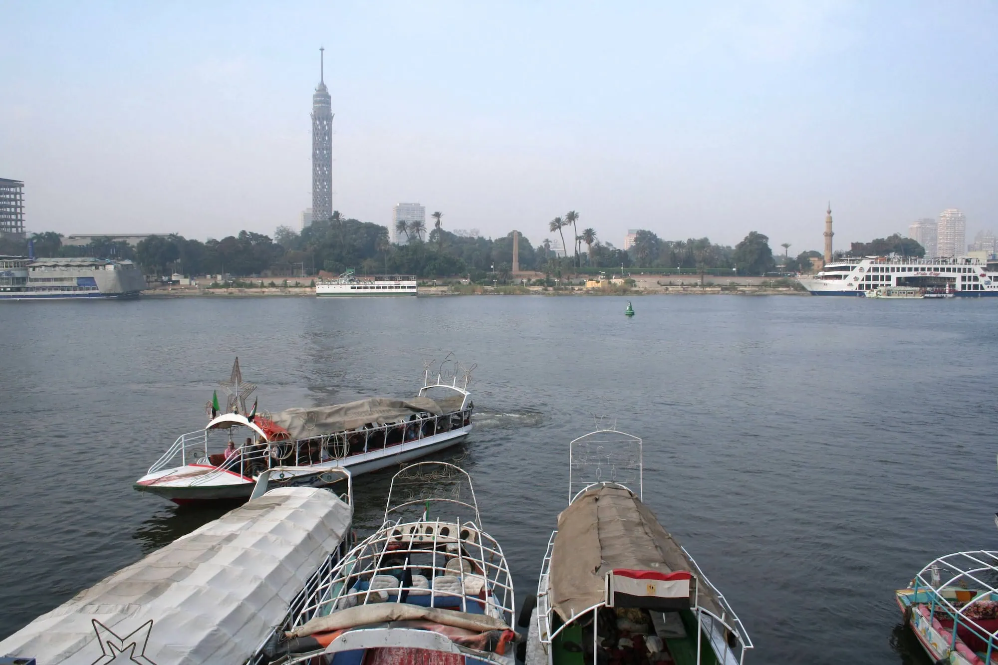 View of Nile River in Cairo with boats docked along riverbank and Cairo Tower in background
