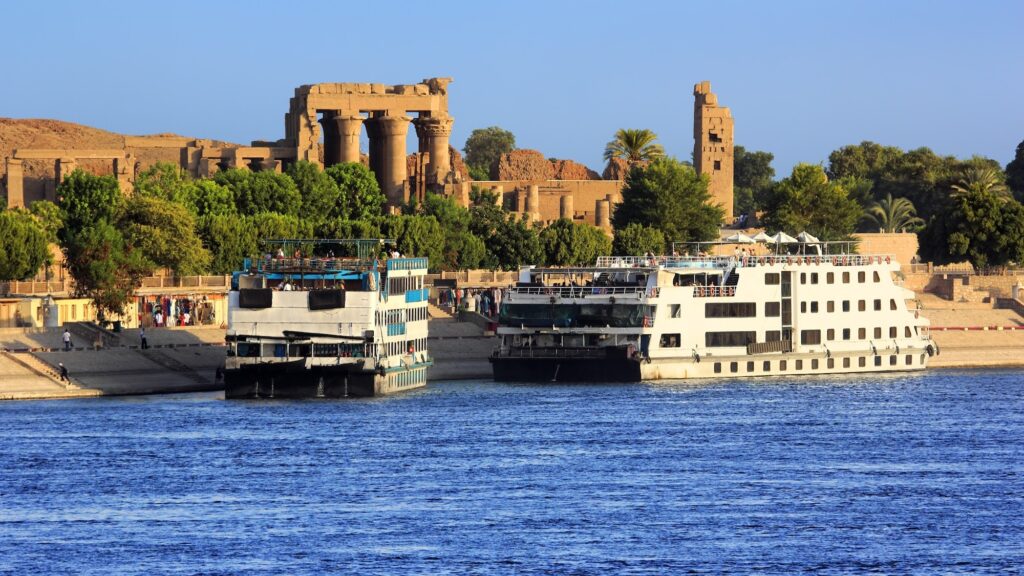 Egypt. Cruise ships docked at Kom Ombo on the Nile. The Temple of Sobek and Haroeris in background seen colonnade of the Hypostyle Hall