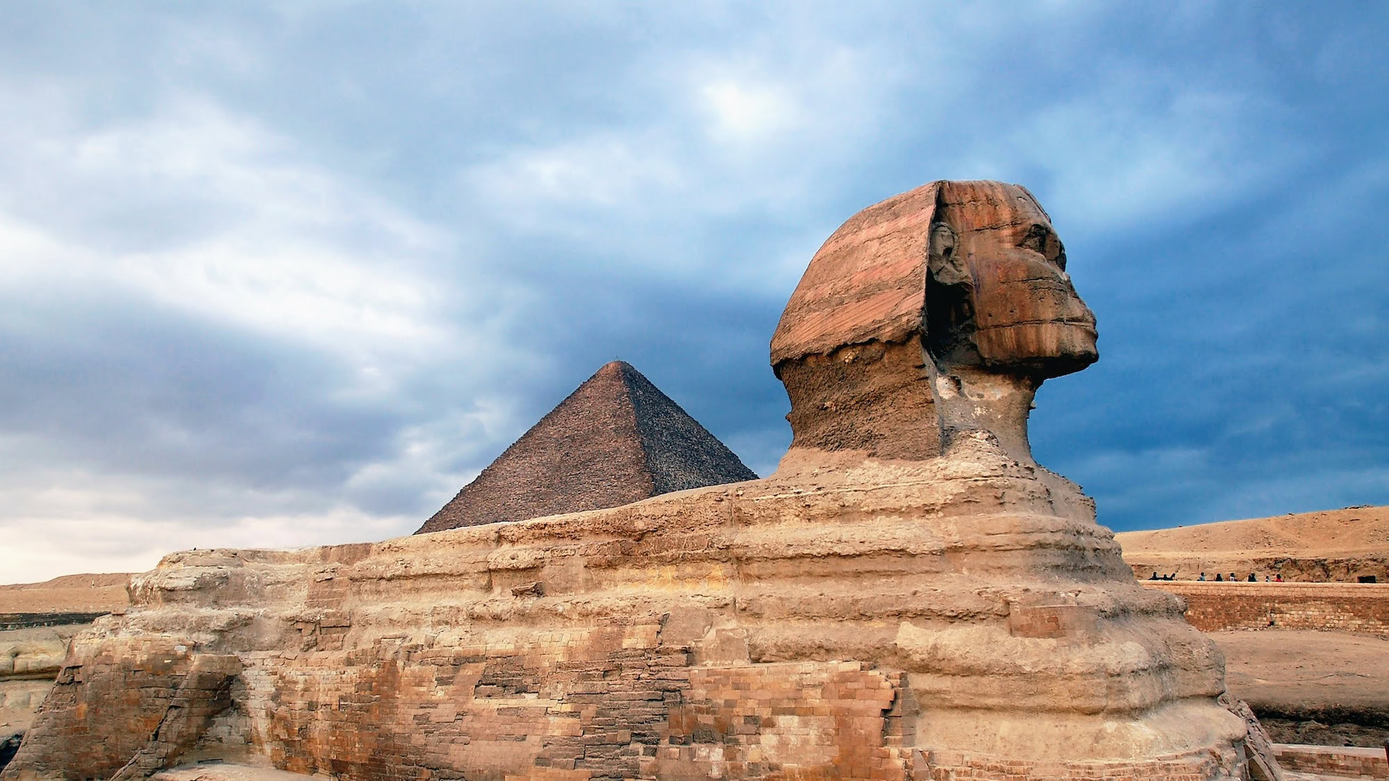 Great Sphinx of Giza with pyramid in background under dramatic cloudy sky