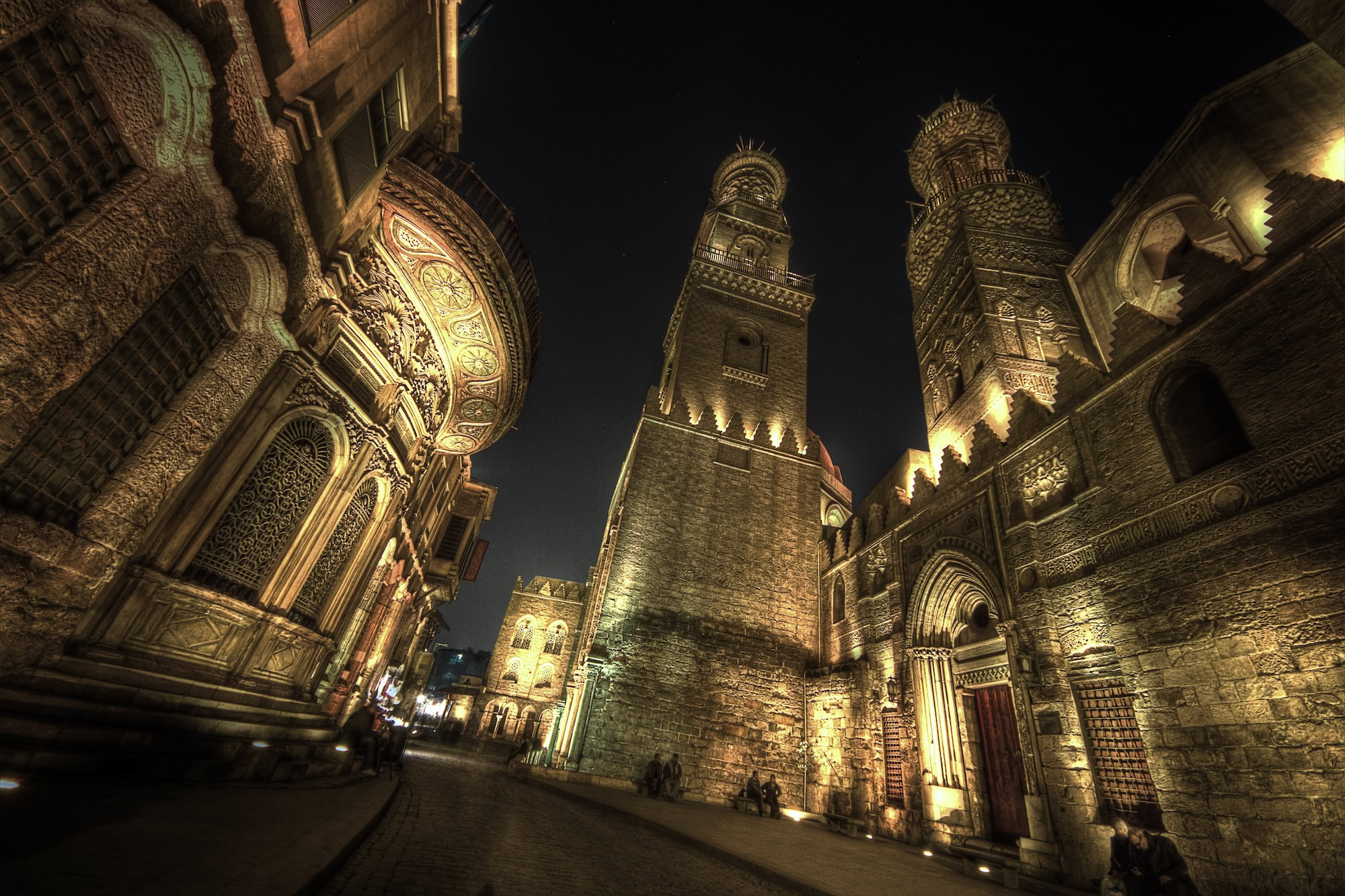 Majestic Islamic mosque in Cairo with ornate minarets, arches, and geometric stonework illuminated at night
