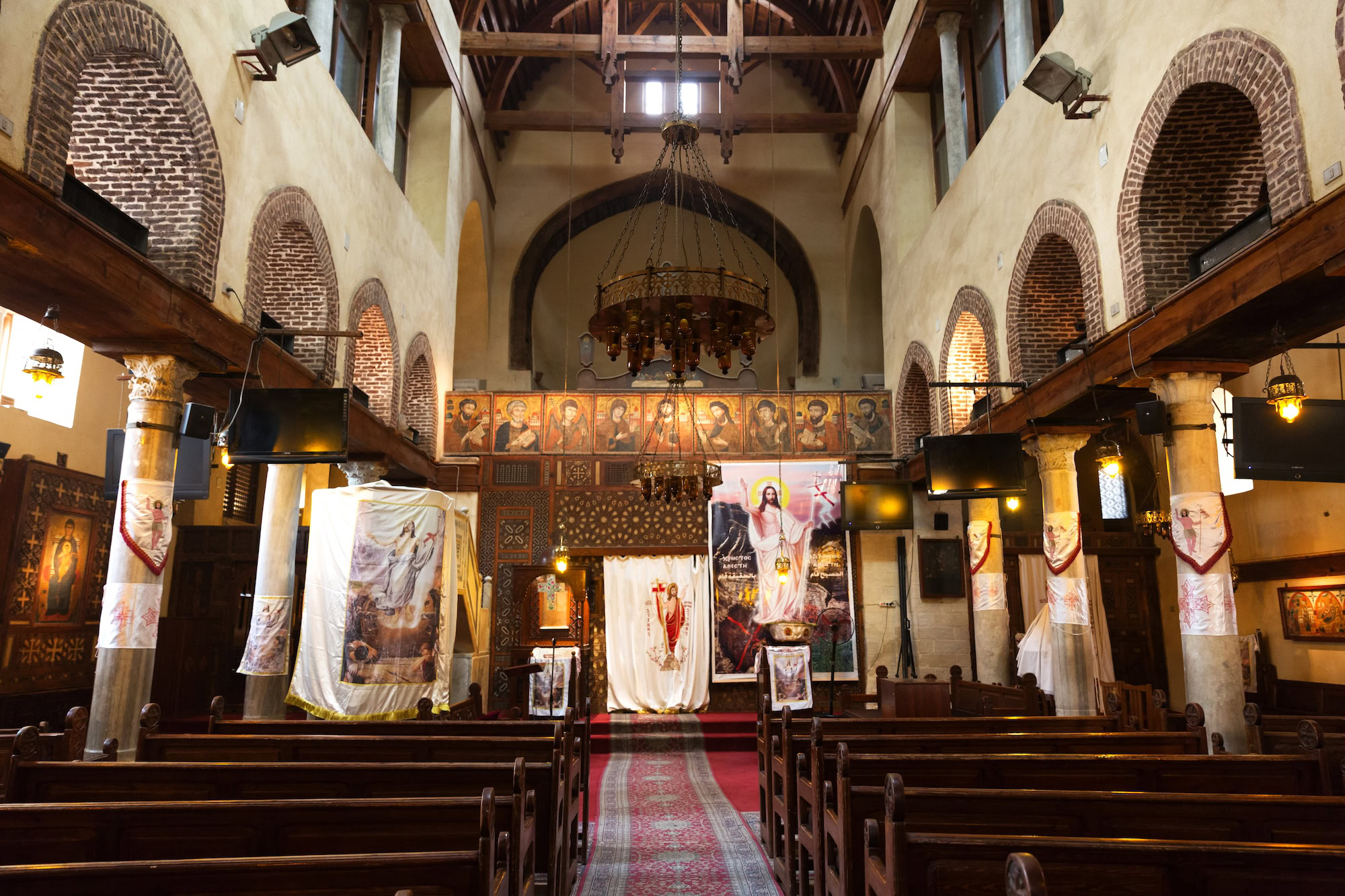 Interior of Coptic Orthodox church with wooden pews, chandelier, and religious decorations