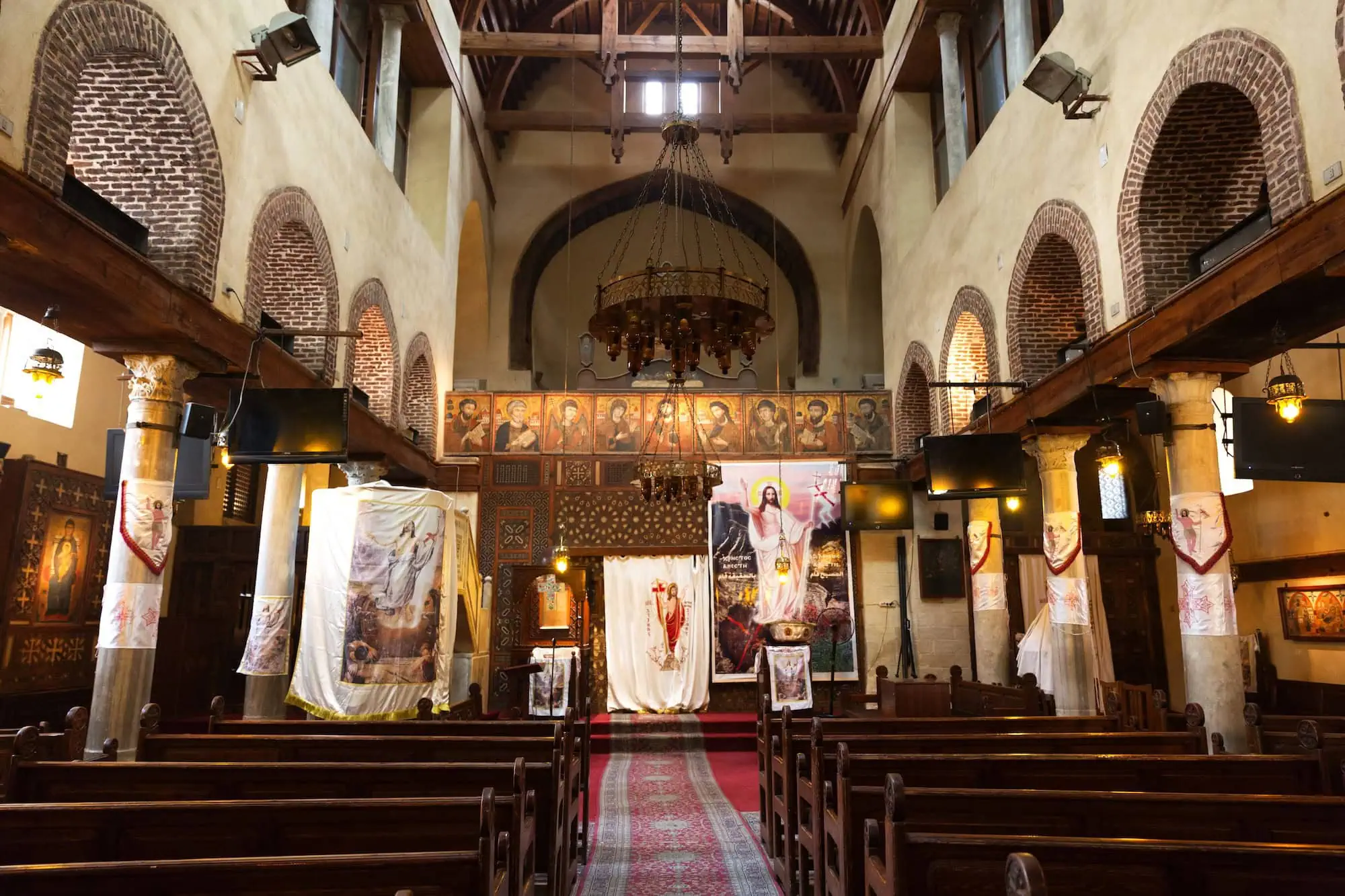 Interior of Coptic Orthodox church with wooden pews, chandelier, and religious decorations