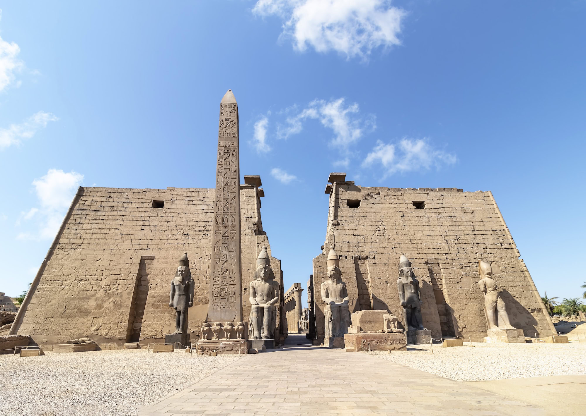 Ancient Luxor Temple entrance with towering obelisk, pharaoh statues, and hieroglyphic-covered stone walls