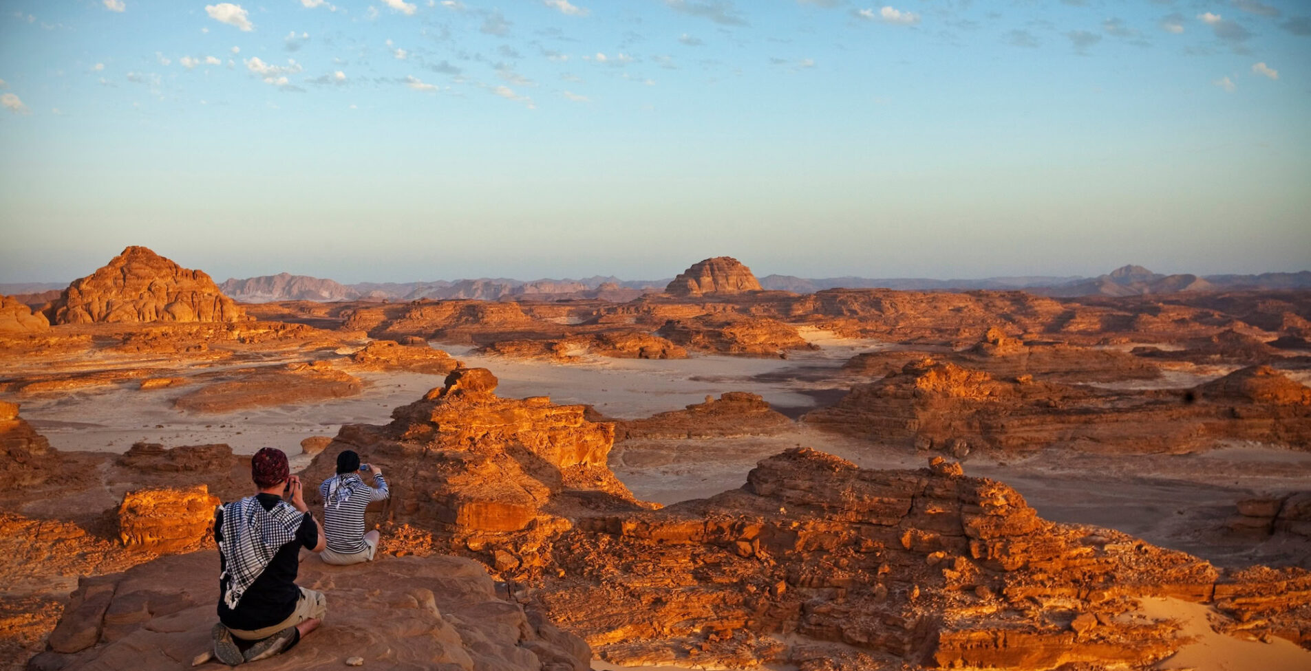 Eroded sand dunes and scattered rock formations beneath a blue sky with white clouds at Sinai Desert South Sinai
