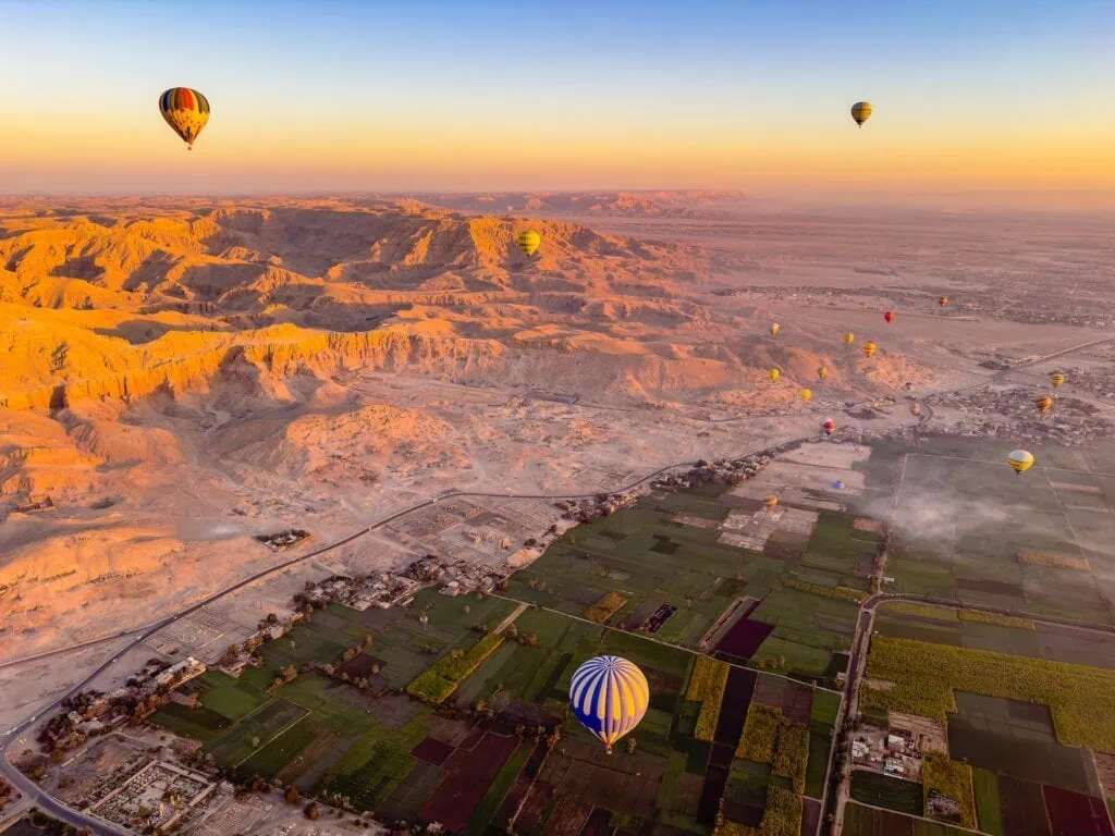 Hot air balloons flying over the Nile Valley with green fields and surrounding desert landscape, Luxor