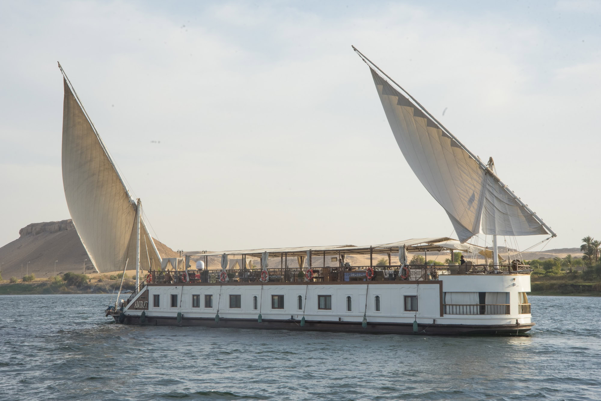 Traditional Egyptian dahabiya sailboat cruising the Nile River with desert landscape backdrop