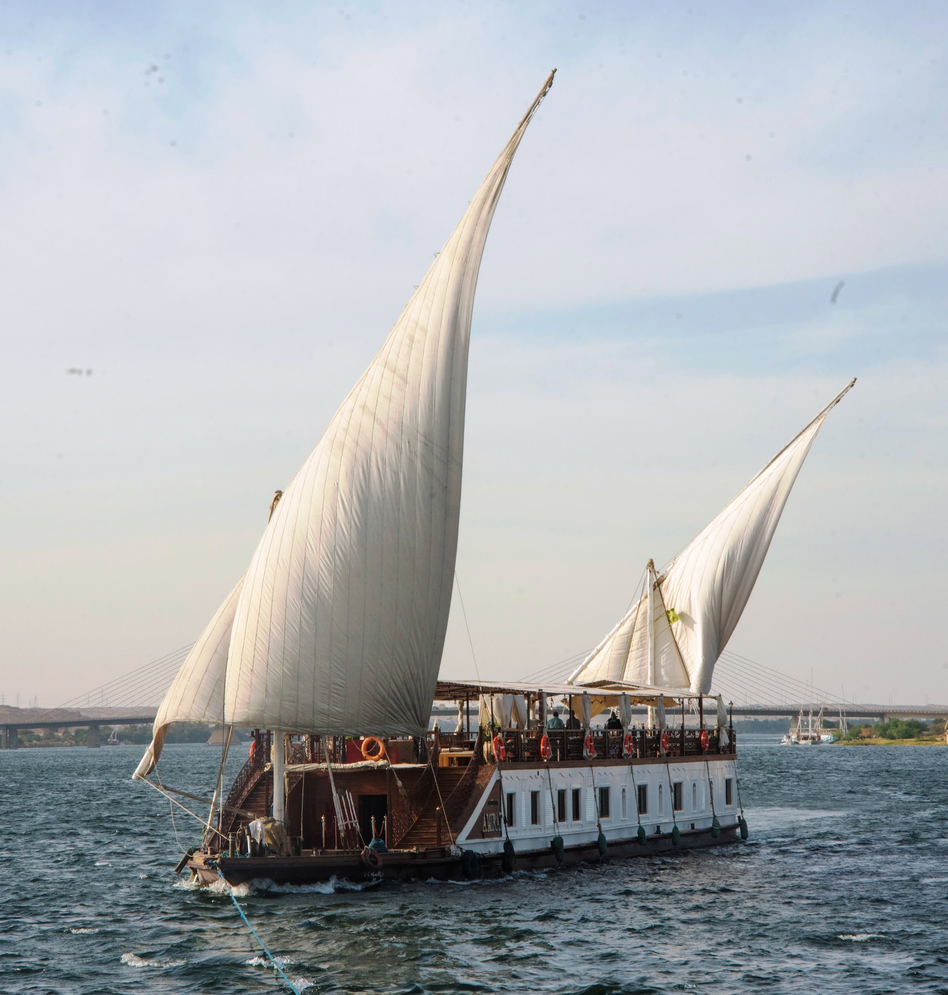 Traditional felucca sailing boat with triangular sails carrying passengers on the Nile River in Egypt