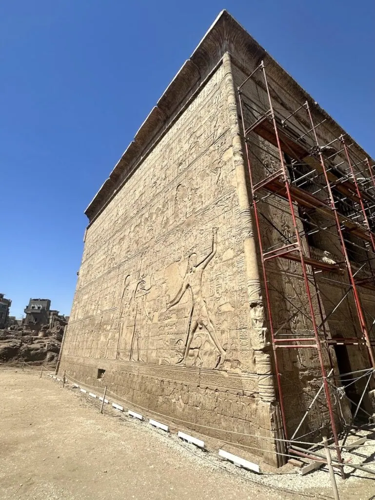 Exterior view of carved stone reliefs and conservation scaffolding at the Temple of Khnum