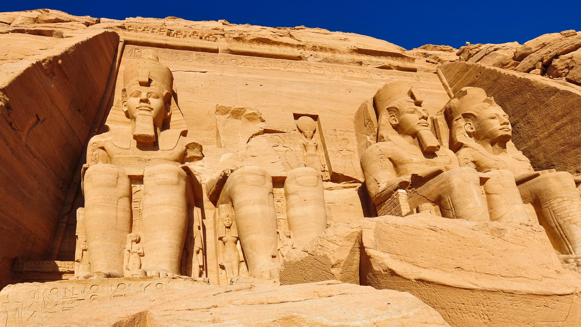 Four colossal seated statues of Pharaoh Ramses II carved into sandstone cliff at Abu Simbel temple