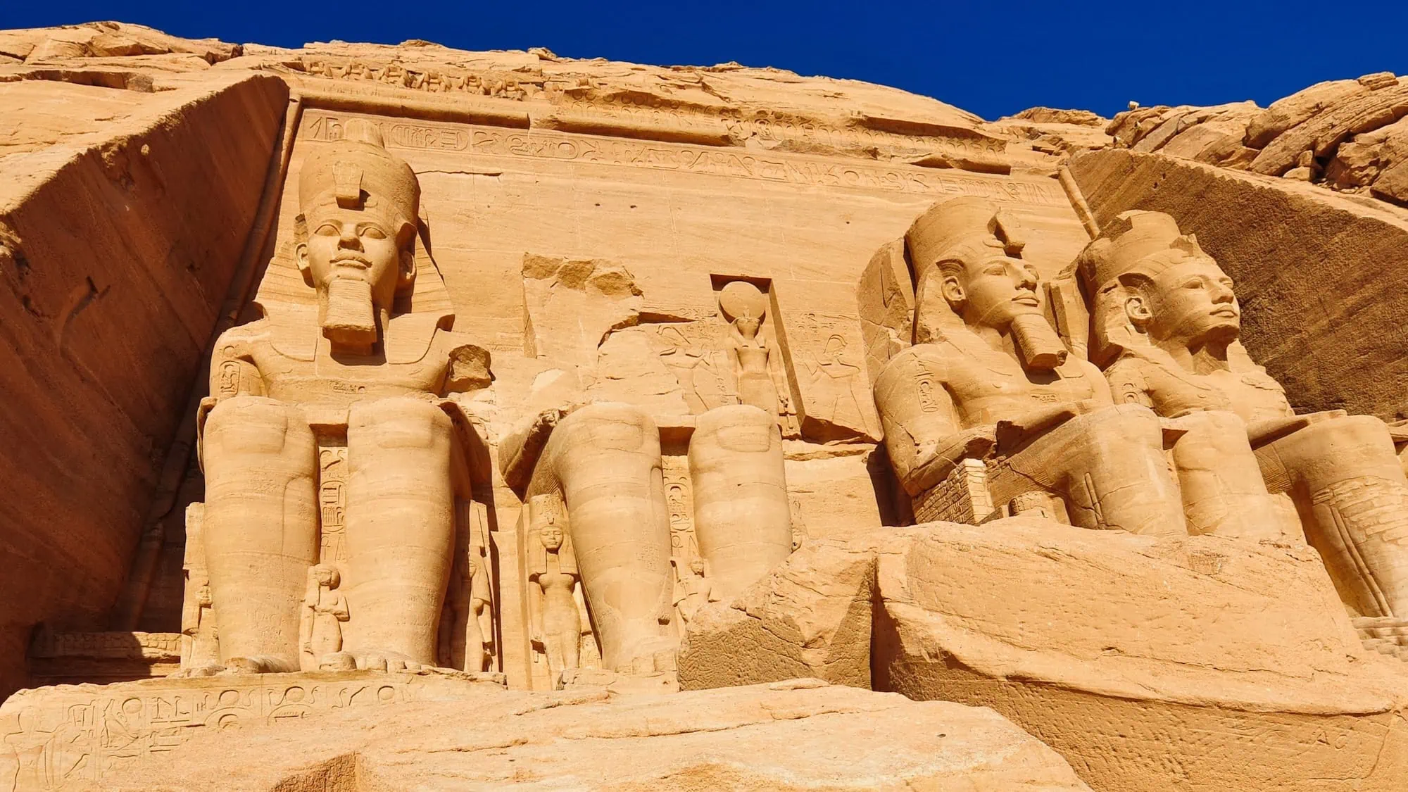 Four colossal seated statues of Pharaoh Ramses II carved into sandstone cliff at Abu Simbel temple