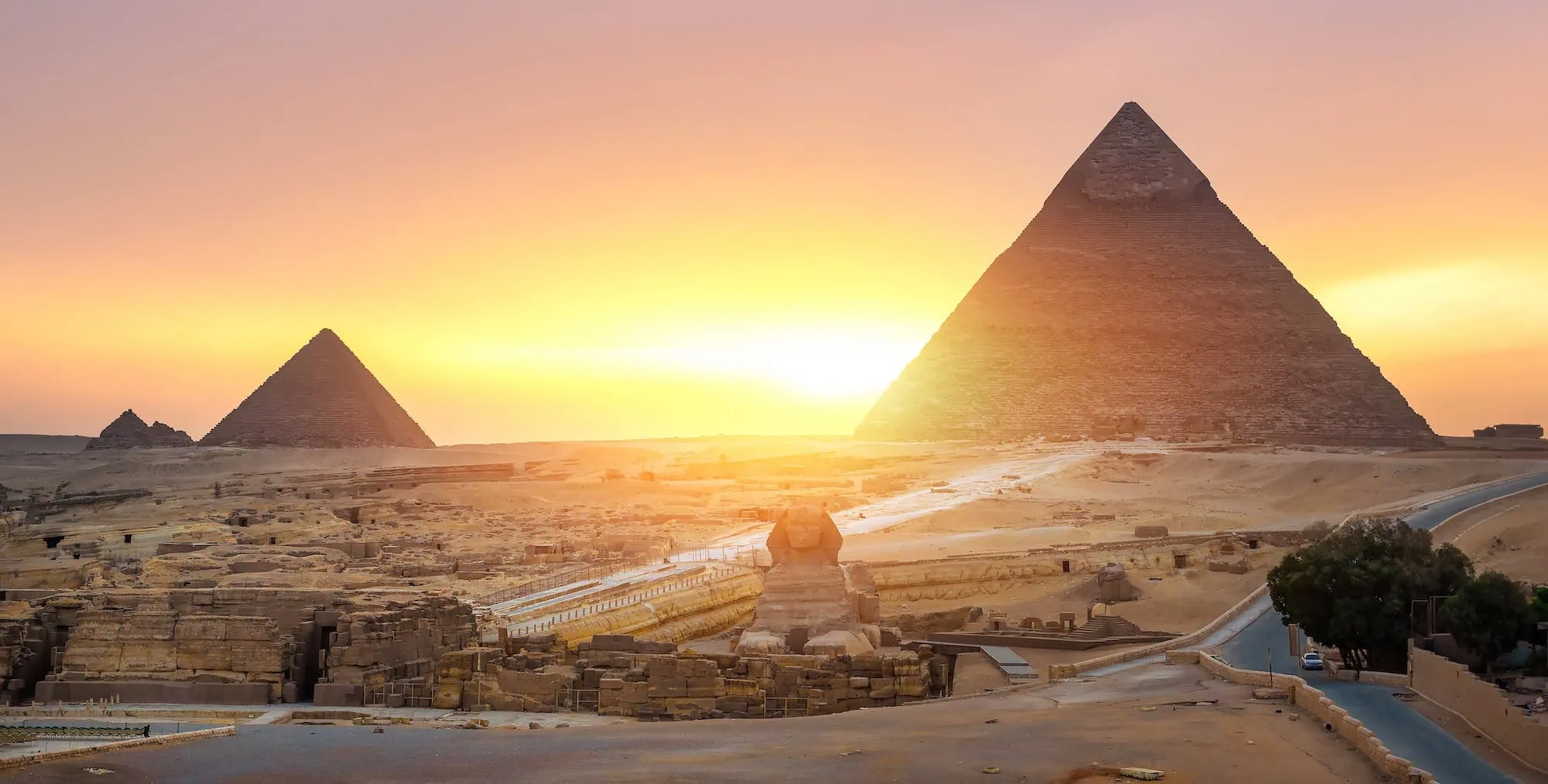 Great Sphinx of Giza in foreground with pyramids at sunset