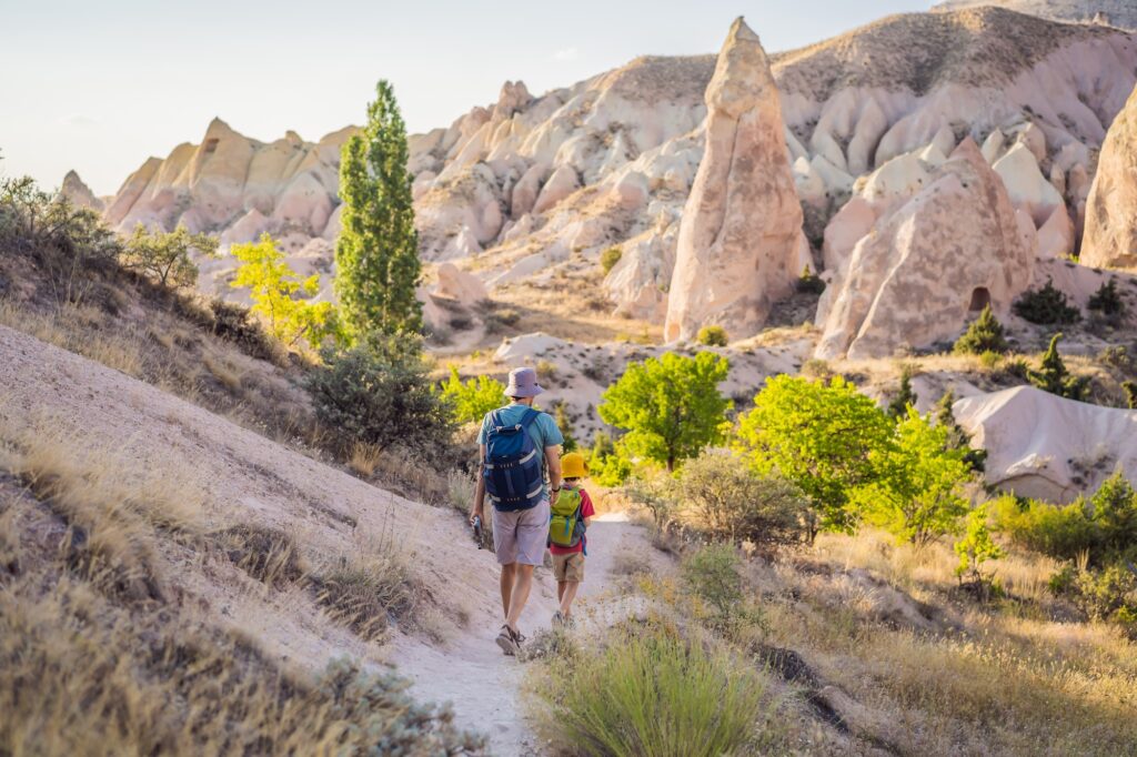 Father and son tourists exploring valley with rock formations and fairy caves near Goreme in Cappadocia Turkey