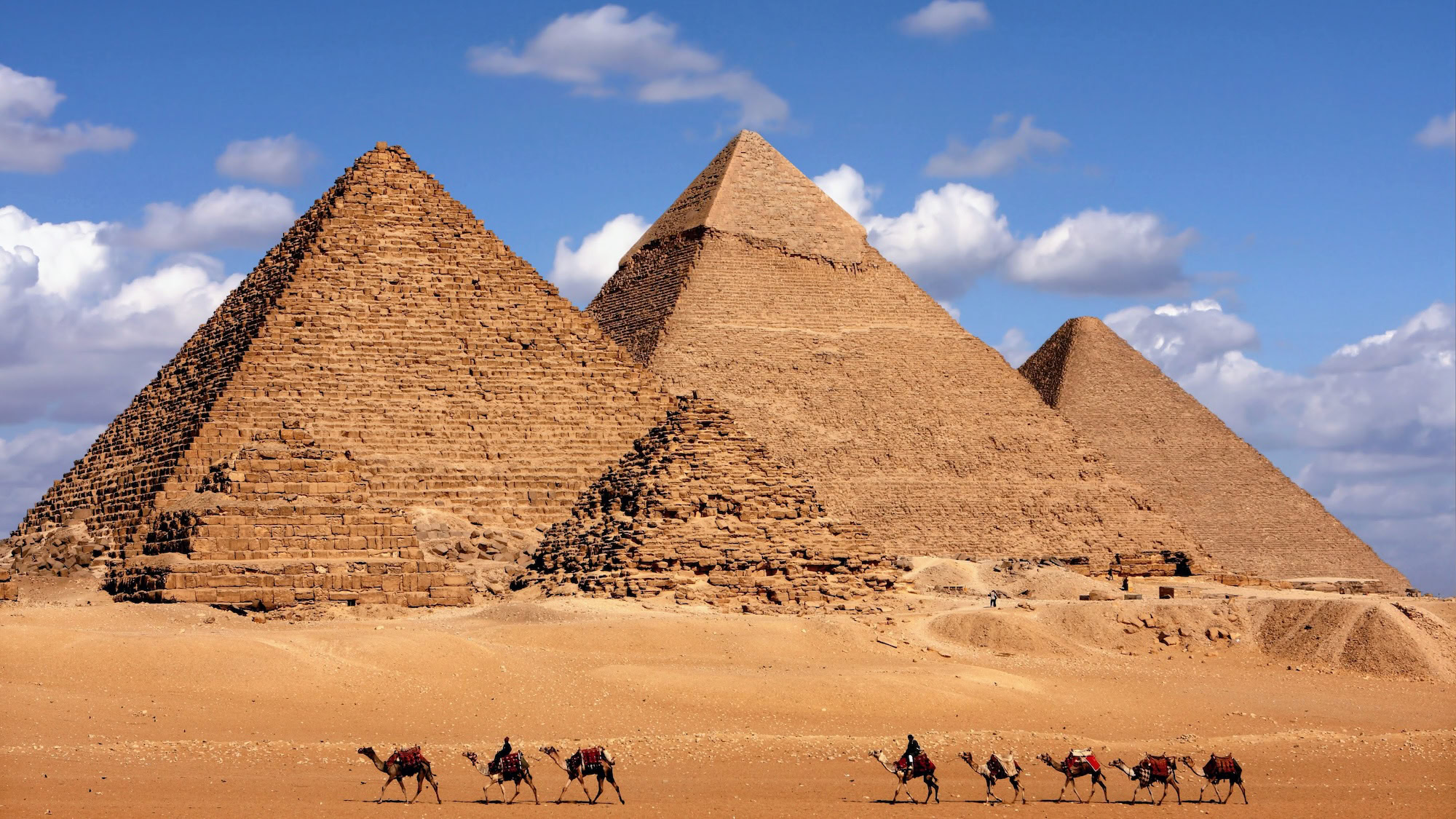 Panoramic view of the three pyramids of Giza with camel caravan in the foreground