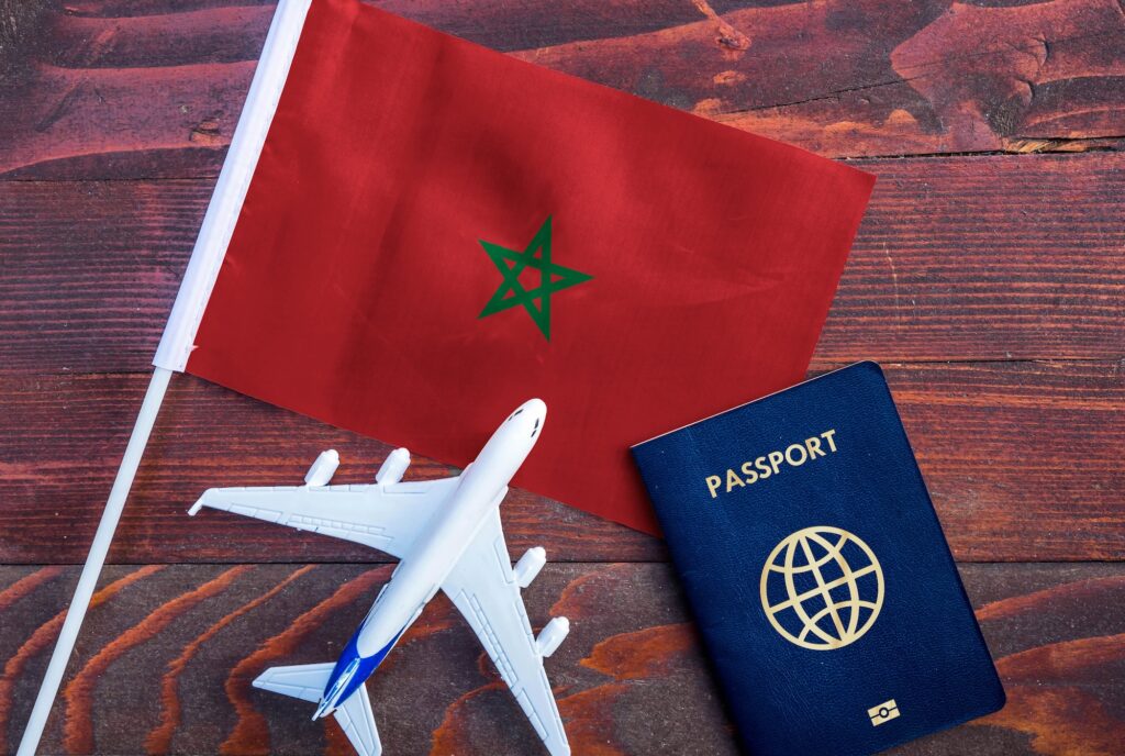 Flag of Morocco with passport and toy airplane on wooden background