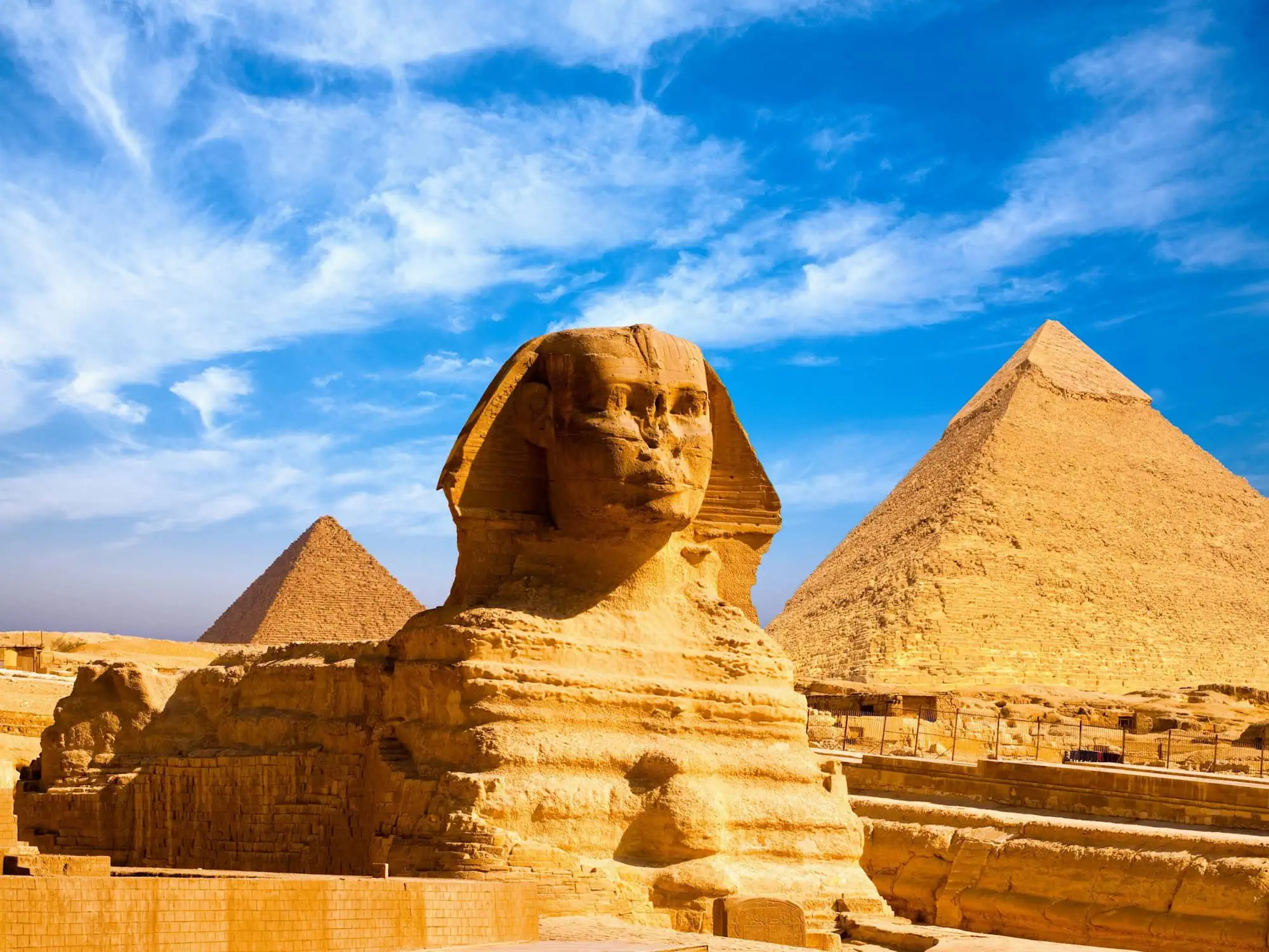 The Great Sphinx of Giza in profile with pyramids visible in the background under a clear blue sky