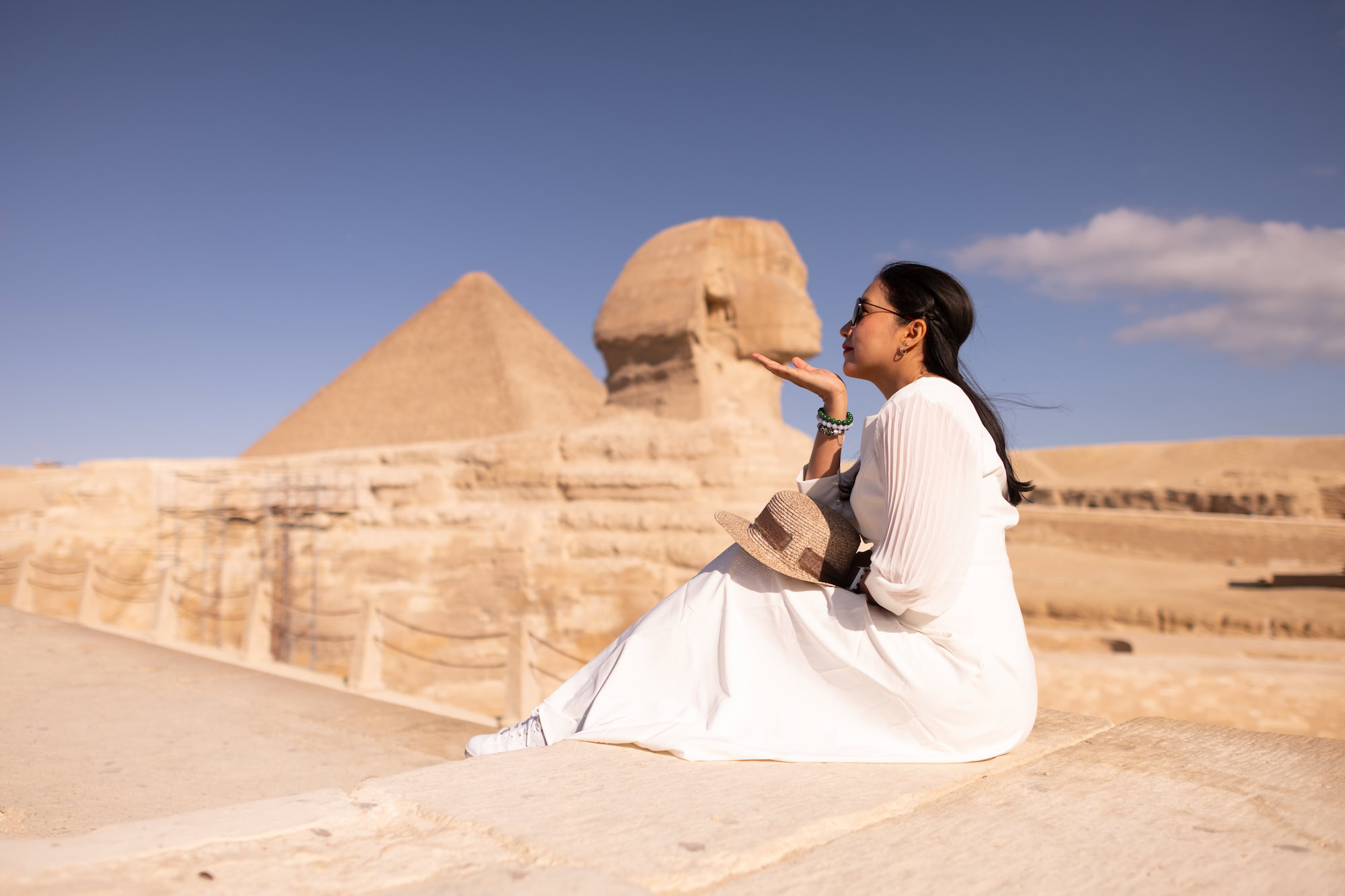 Woman in white dress and hat standing near the Great Sphinx and Pyramid of Giza