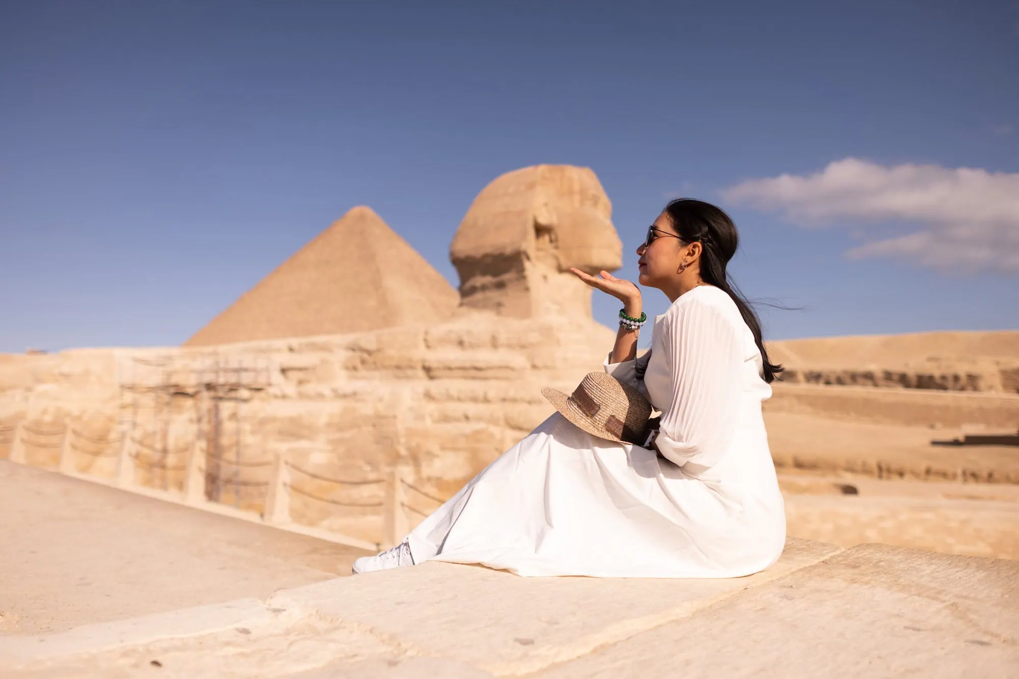 Woman in white dress and hat standing near the Great Sphinx and Pyramid of Giza