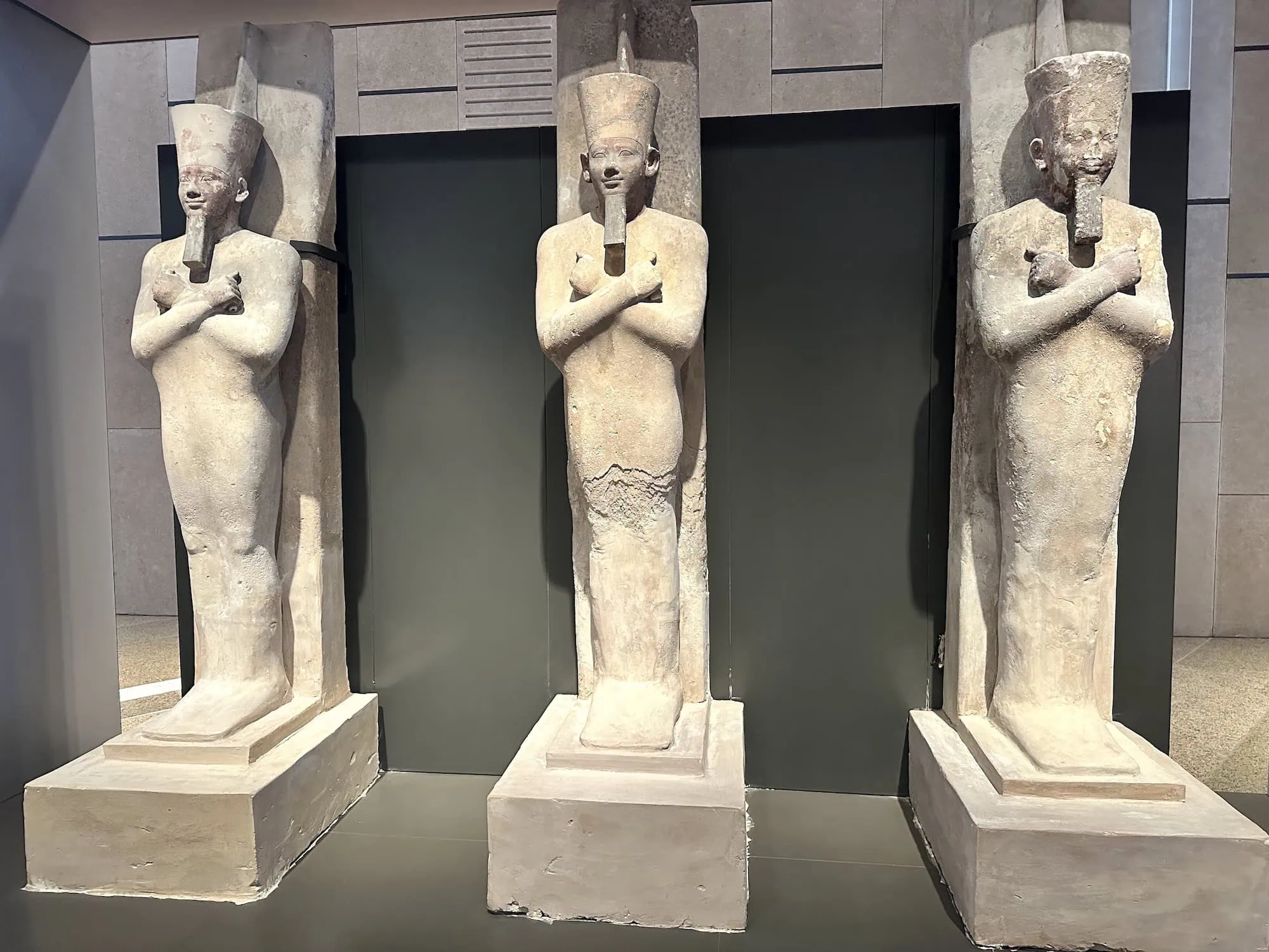 Three ancient Egyptian sarcophagi displayed on pedestals in the Grand Egyptian Museum