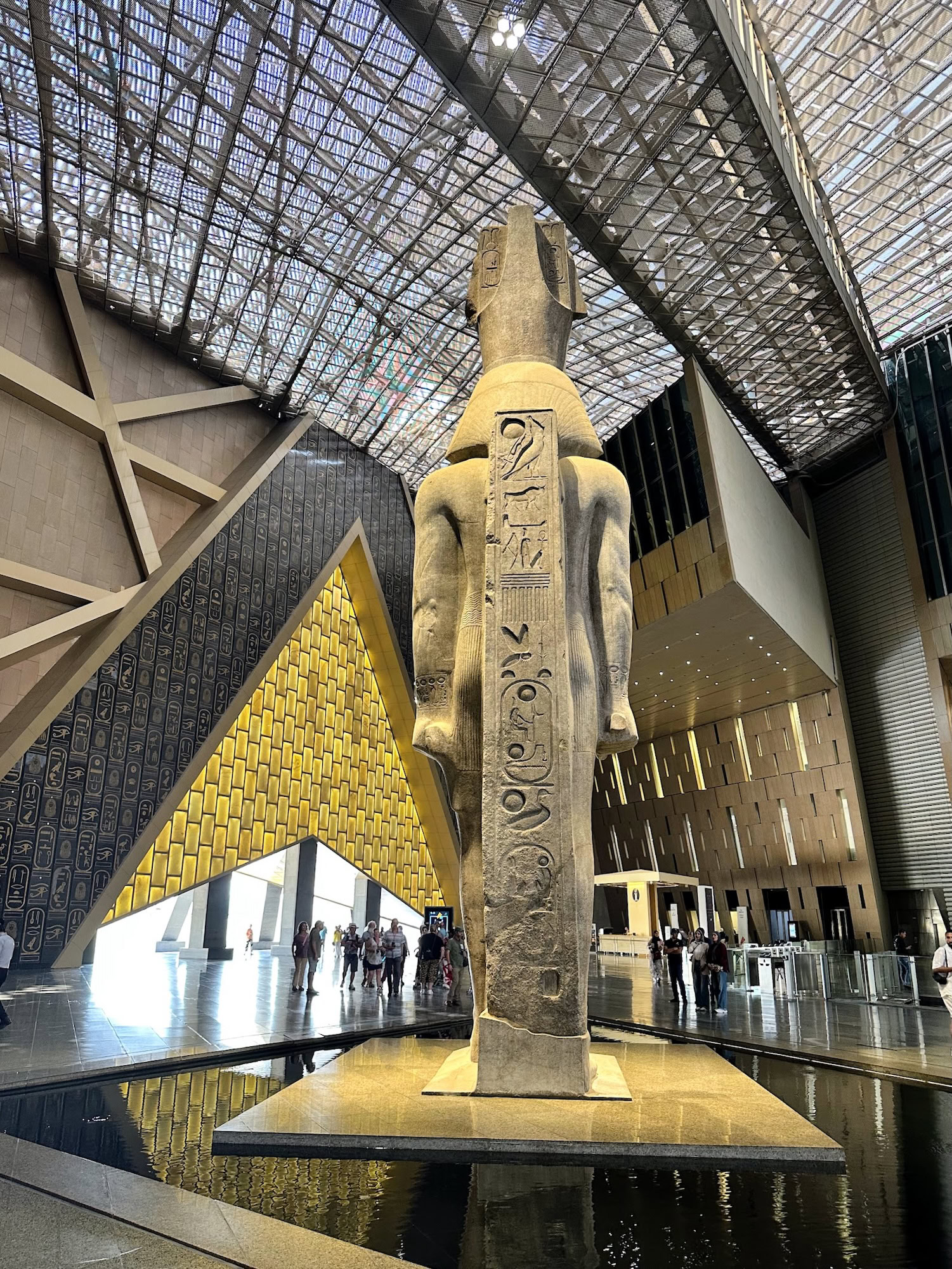 Interior of Grand Egyptian Museum showing ancient Egyptian statue with hieroglyphics and modern glass architecture