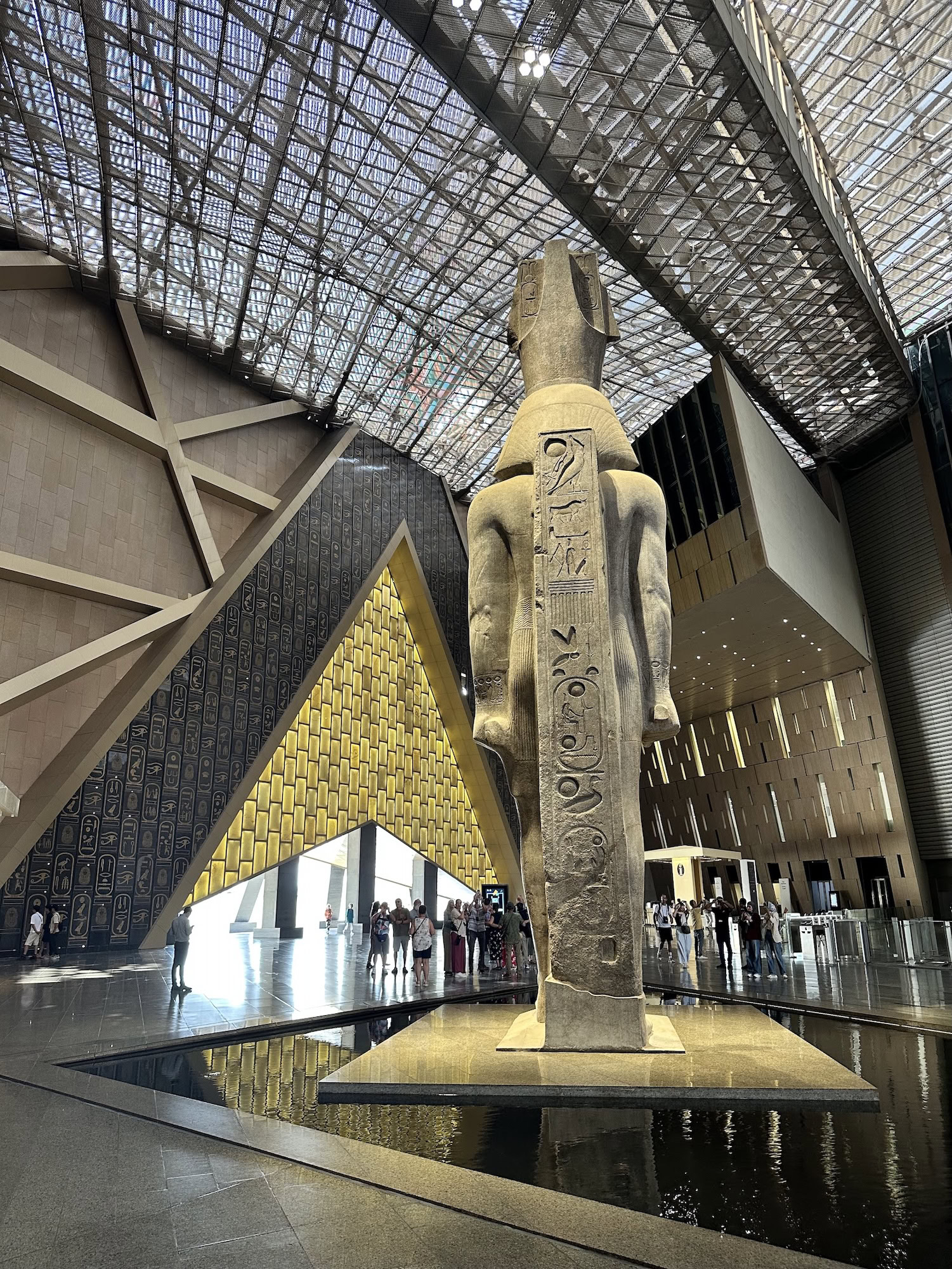 Interior of Grand Egyptian Museum with ancient Egyptian statue, hieroglyphs, and modern glass ceiling architecture