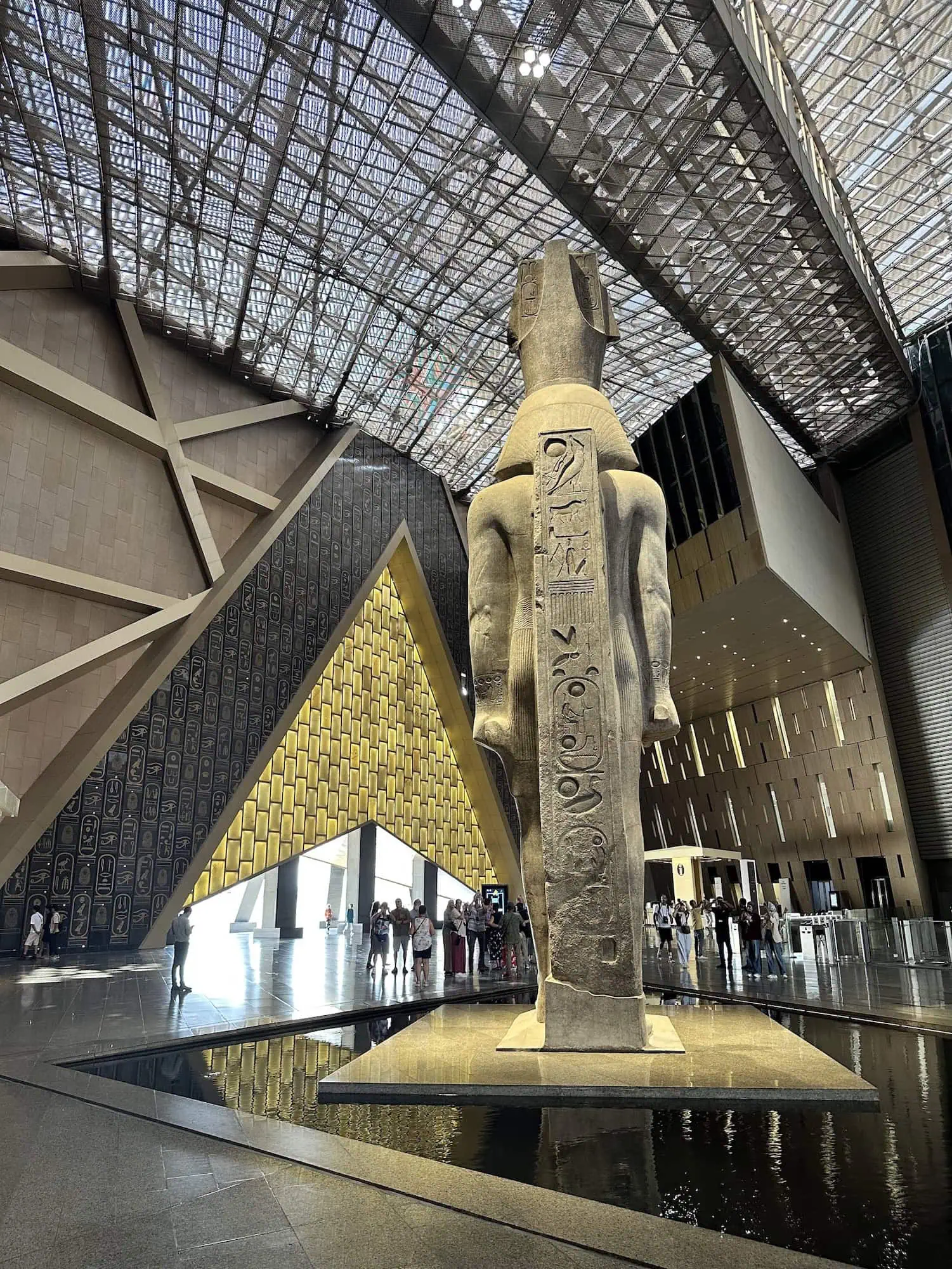 Interior of Grand Egyptian Museum with ancient Egyptian statue, hieroglyphs, and modern glass ceiling architecture