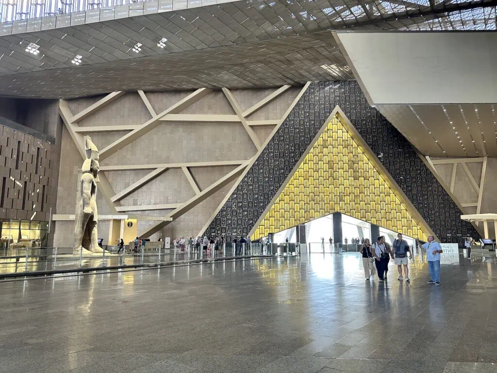 Spacious interior with high glass walls, polished floors, and large ancient statues displayed in the Grand Egyptian Museum Main Hall, Giza