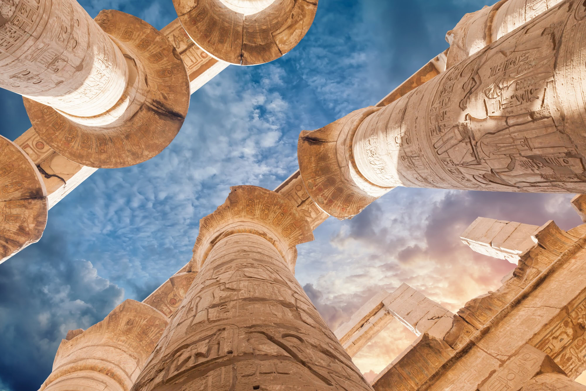 Majestic stone columns of Karnak Temple with hieroglyphics under golden sky