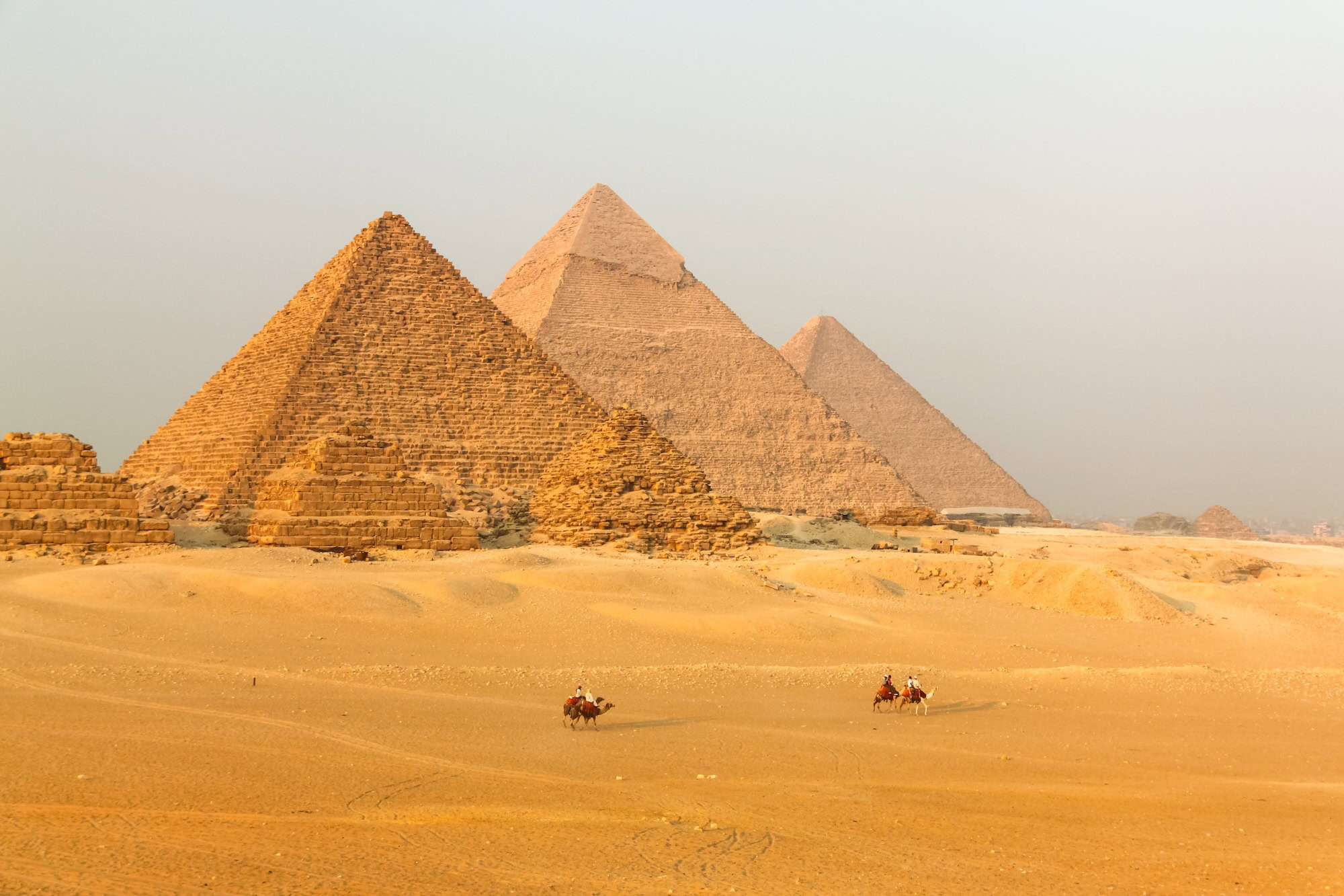 The three pyramids of Giza in Egypt with camel riders crossing golden desert sands