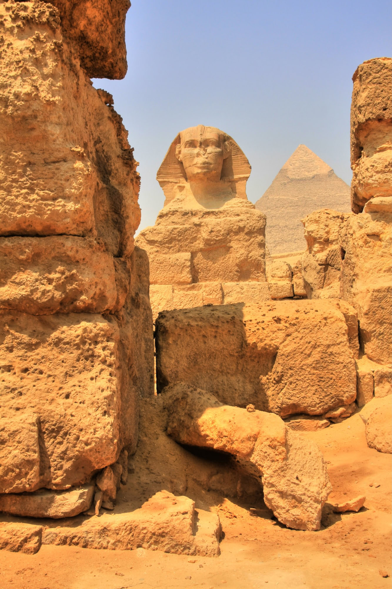 Great Sphinx of Giza with pyramid in background viewed through ancient stone ruins