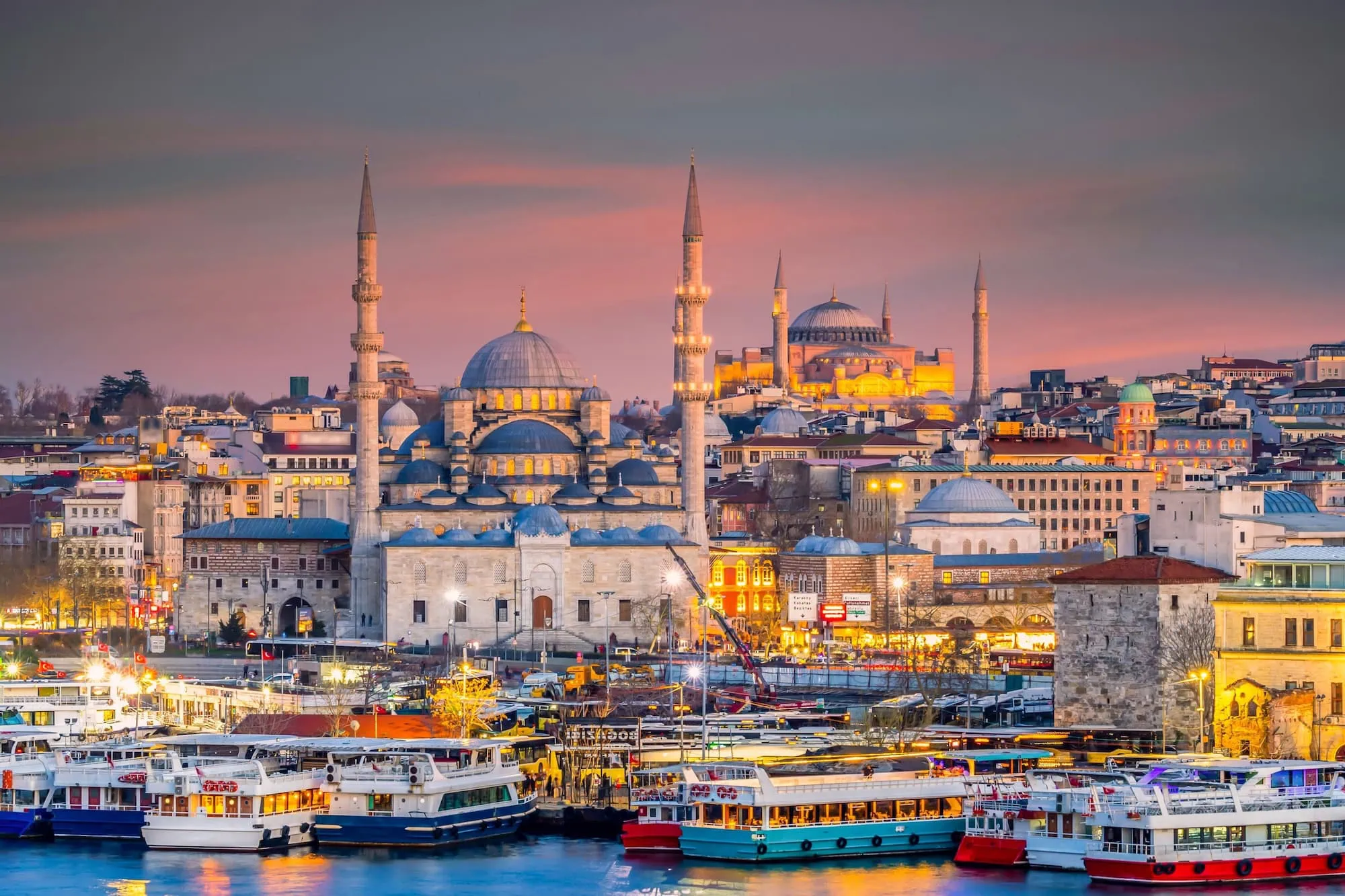 Twilight view of illuminated Hagia Sophia mosque overlooking Istanbul's historic harbor with boats