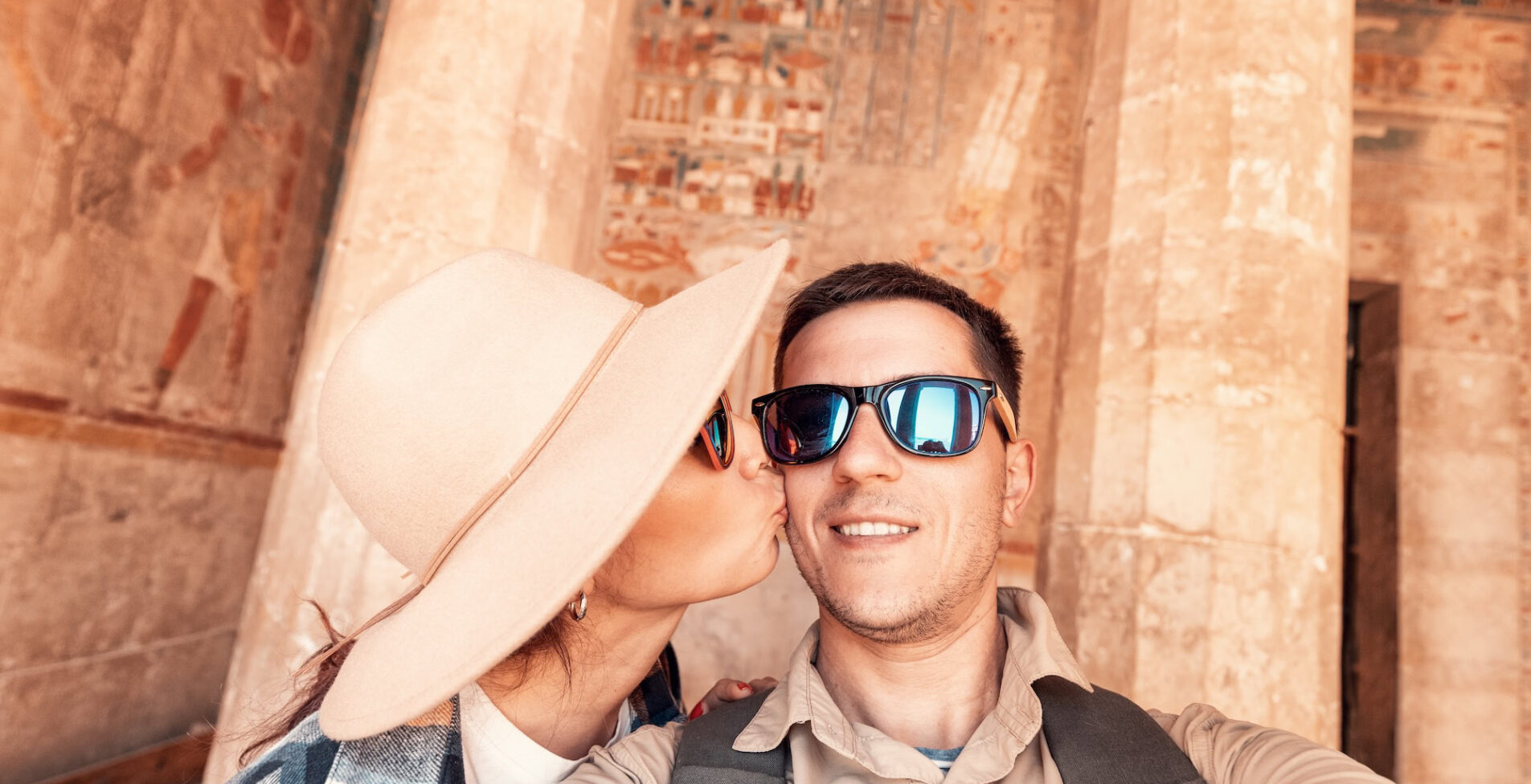 Happy traveler couple in love takes a selfie photo and kissing inside Hatshepsut Temple in Luxor during the honeymoon tour in Egypt