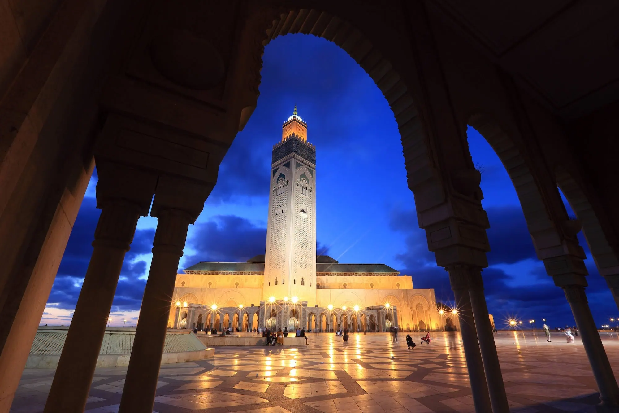 Hassan II Mosque in Casablanca at twilight, with illuminated minaret viewed through decorative arches