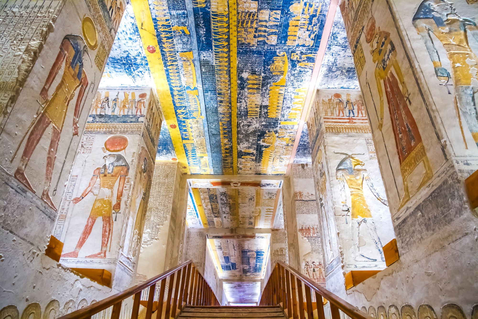 Interior of ancient Egyptian tomb showing colorful hieroglyphics and wall paintings on ceiling and walls
