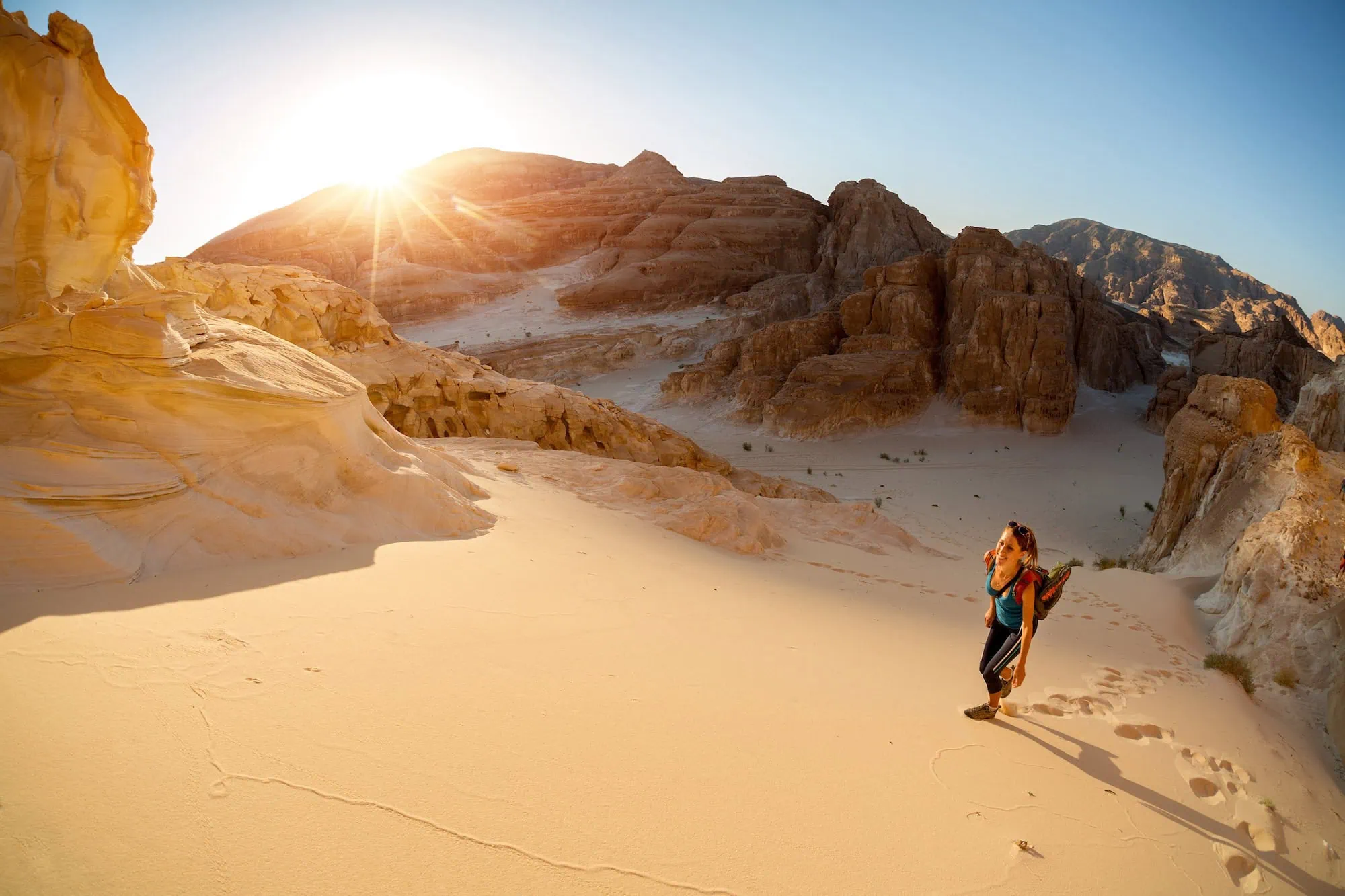 Hiker walking through Wadi Rum desert with dramatic sandstone cliffs and rock formations