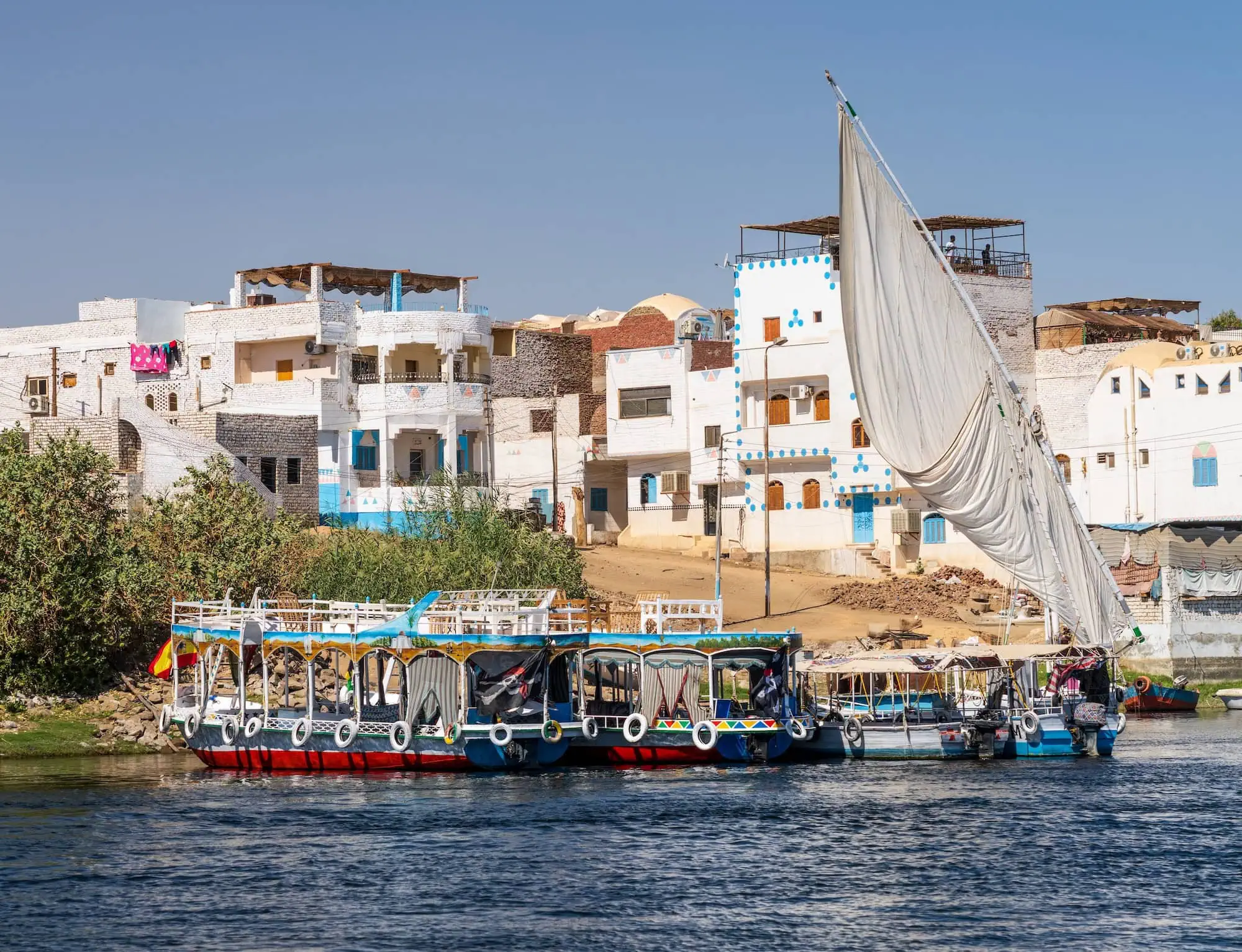 Traditional Nile waterfront village with felucca sailboat and colorful houses along the riverbank