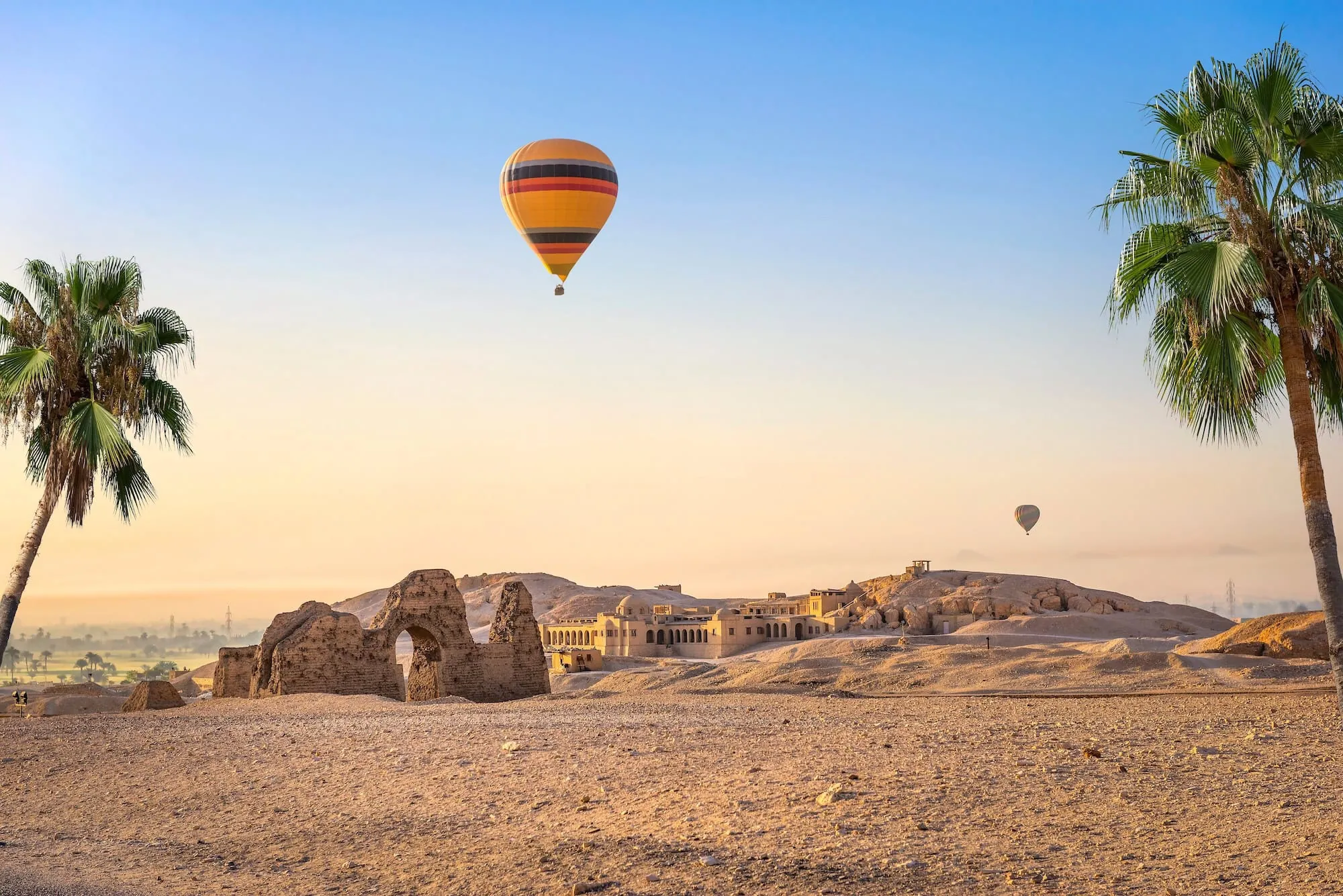 Hot air balloon floating over Valley of the Kings desert landscape with ancient ruins