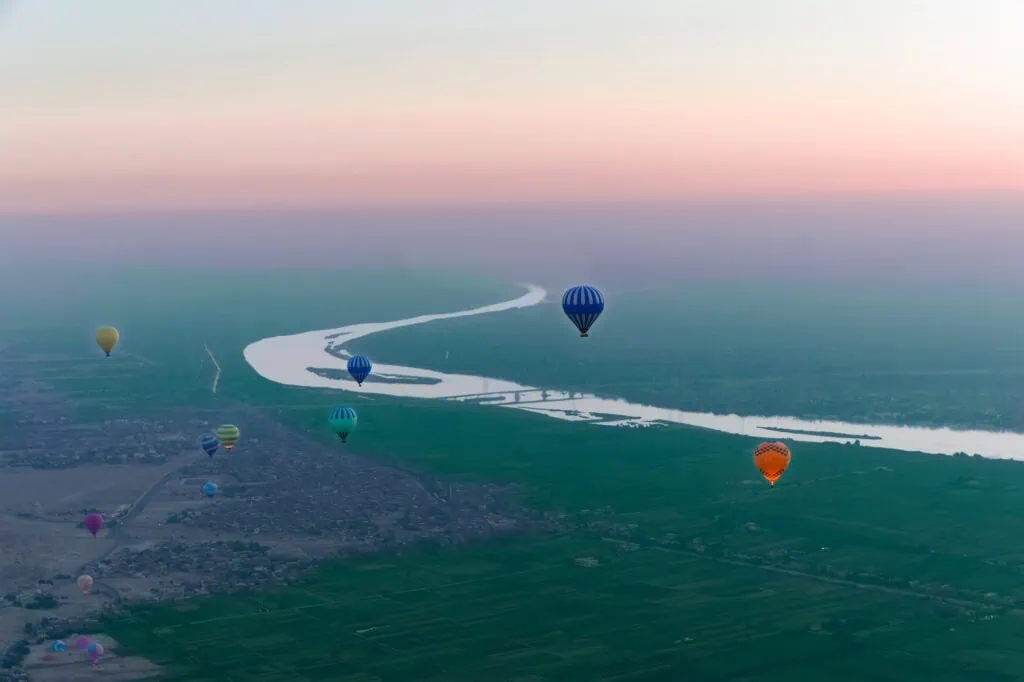 Hot air balloons drifting above the West Bank and the Nile River with green fields along the riverbanks, West Bank, Luxor